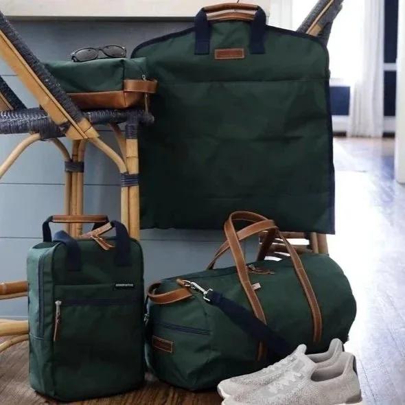 Set of travel bags, a backpack, duffle bag, and garment bag, along with a pair of gray sneakers, arranged indoors near a wooden chair and a window.