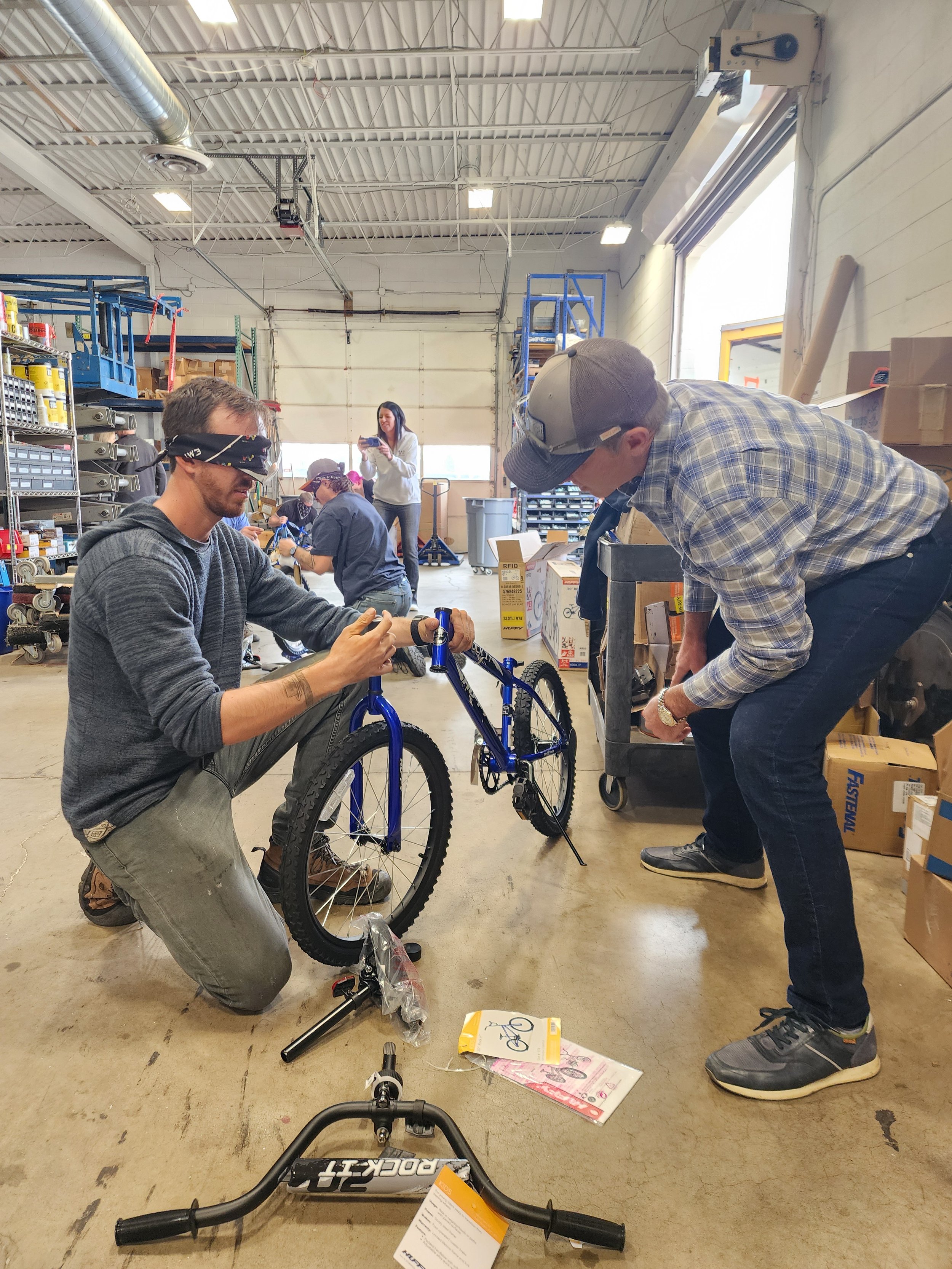 One employee guiding his blindfolded teammate through building a bike at a Wish for Wheels corporate team building event.