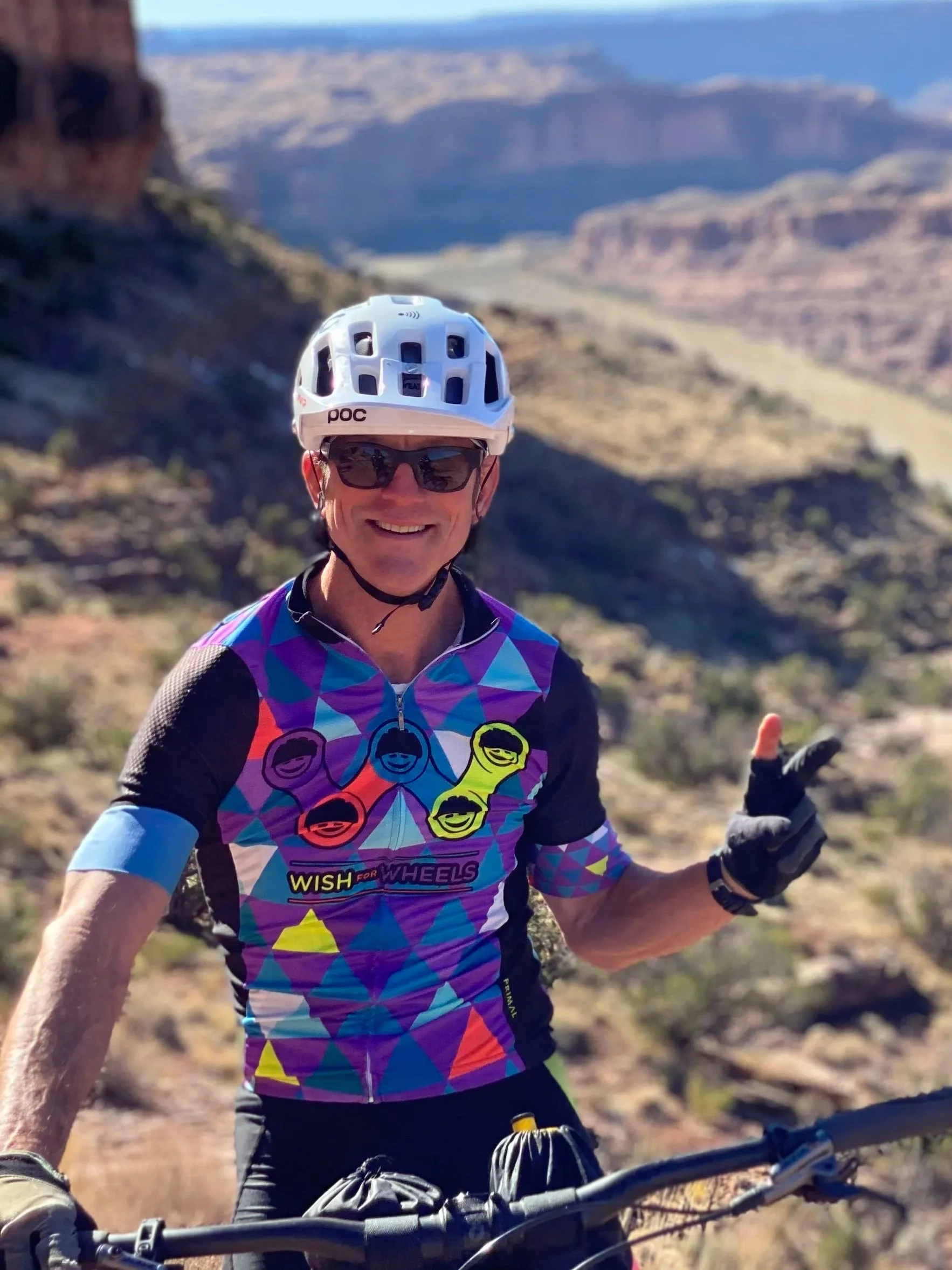 Greg Greenwood, CEO/Executive Director of Wish for Wheels on a bike in front of a beautiful landscape.