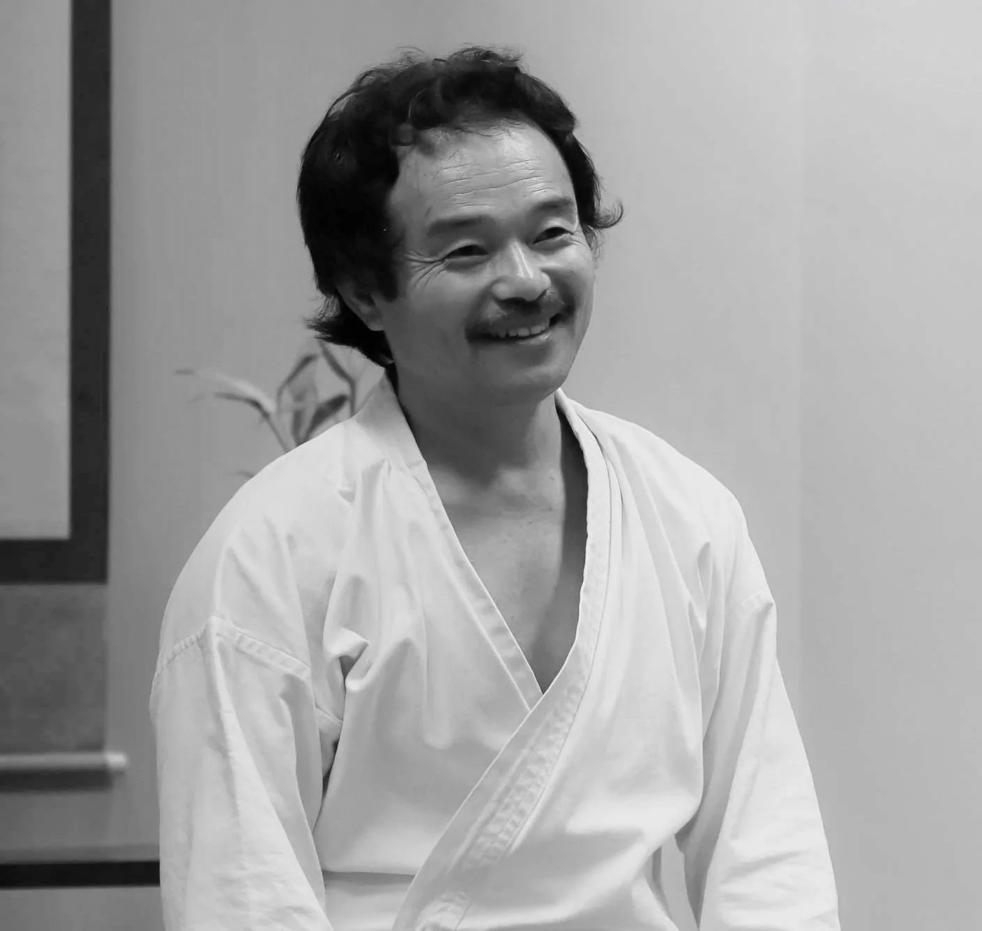 Homem sorridente vestindo uniforme de artes marciais em uma sala interna.