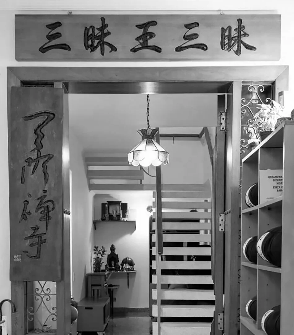 Entrada decorada de uma casa com painel em letras japonesas, escada de madeira, luminária de teto e decoração oriental ao fundo.