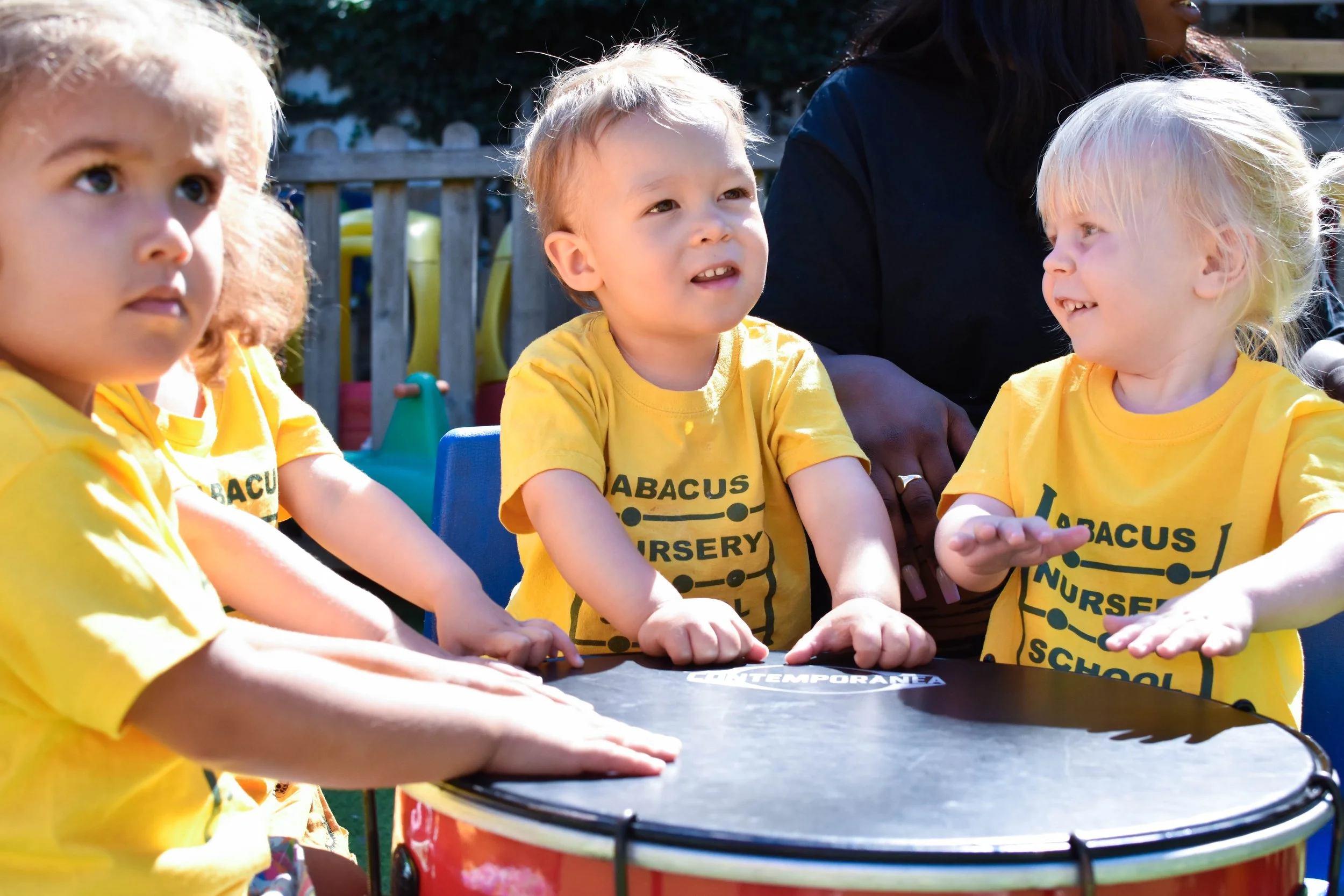 Children playing drums together during an outdoor creative learning session at Abacus Nursery School