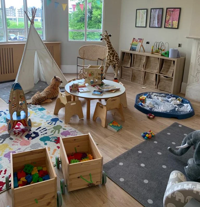 Toddler standing at wooden table with toy cars and books in a bright room
