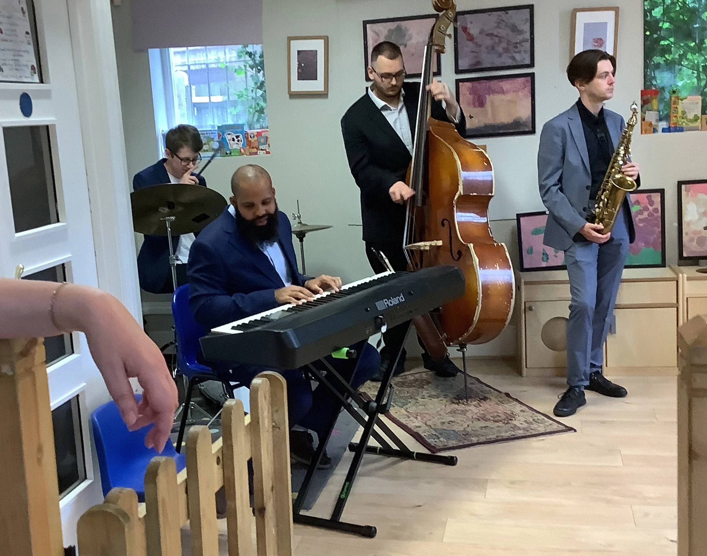 A jazz trio with a piano, double bass, and saxophone performing at a nursery community event at Abacus Nursery School
