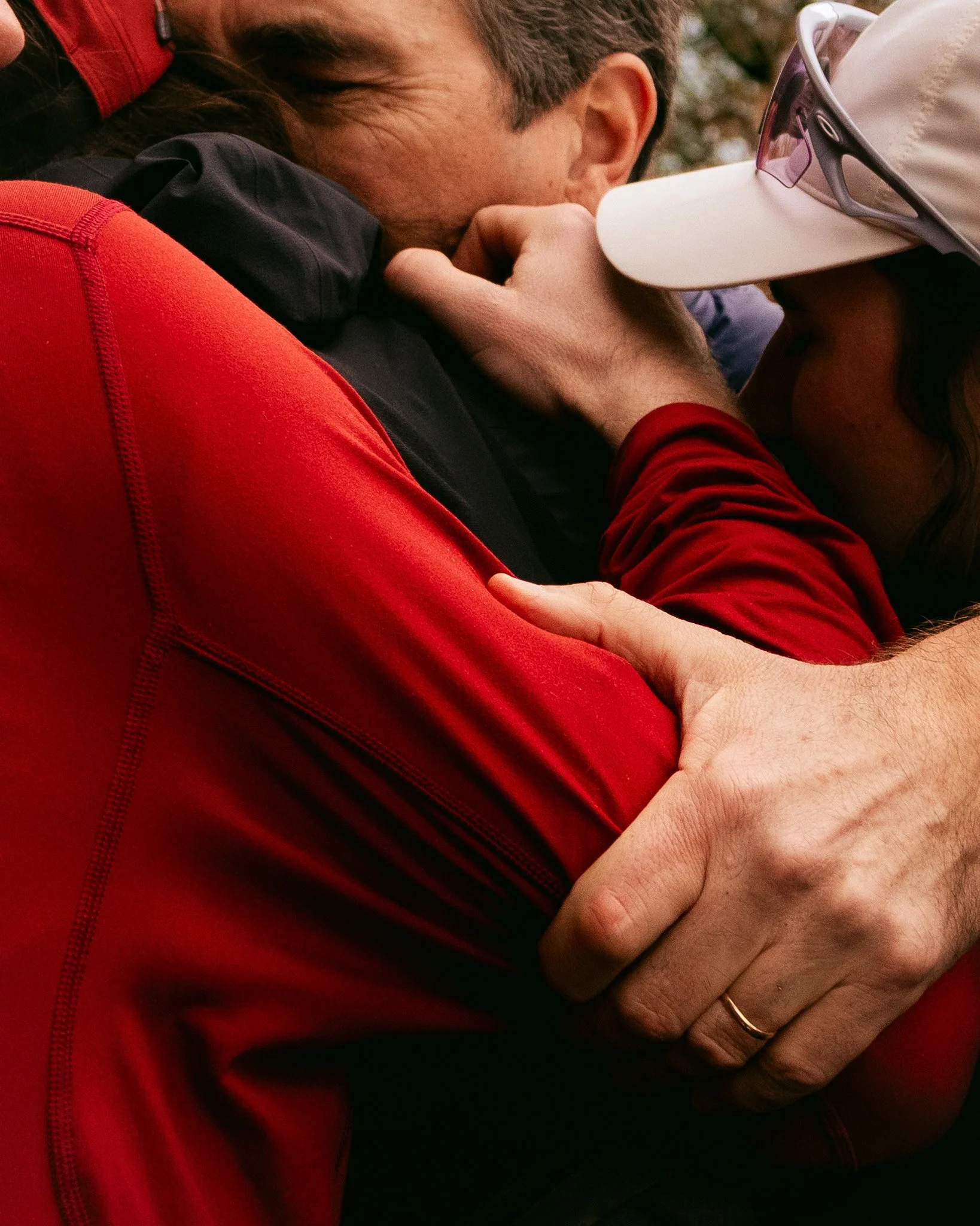 Deux personnes s'embrassent tendrement, l'une porte une casquette blanche et des lunettes de soleil, l'autre porte une veste rouge.