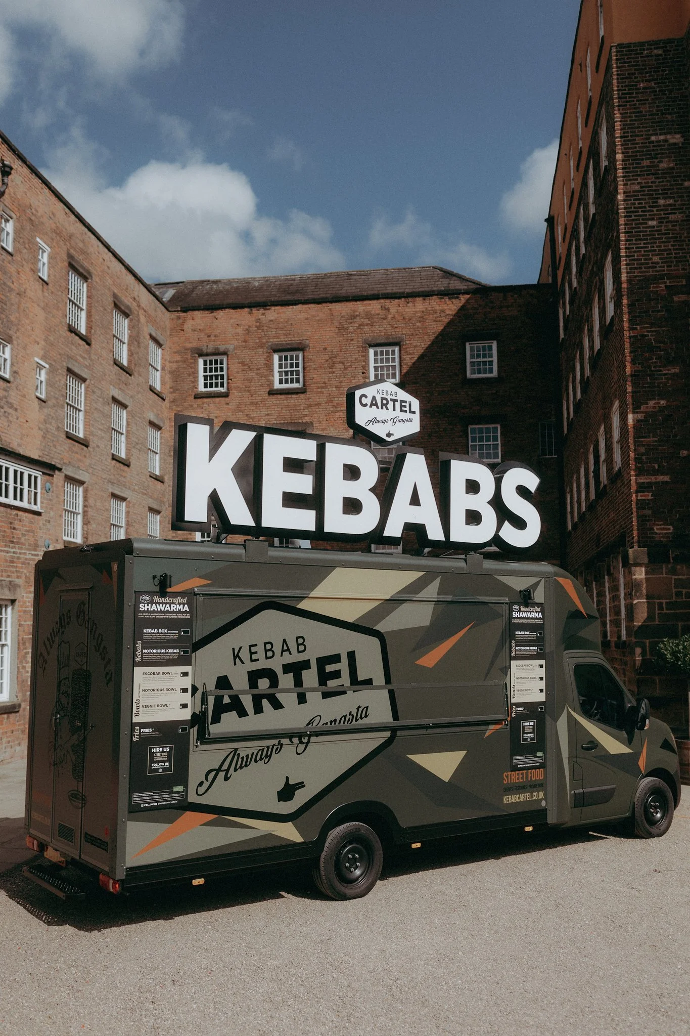 Food truck labeled 'Kebab Cartel' parked in a brick courtyard with a large 'KEBABS' sign on top.