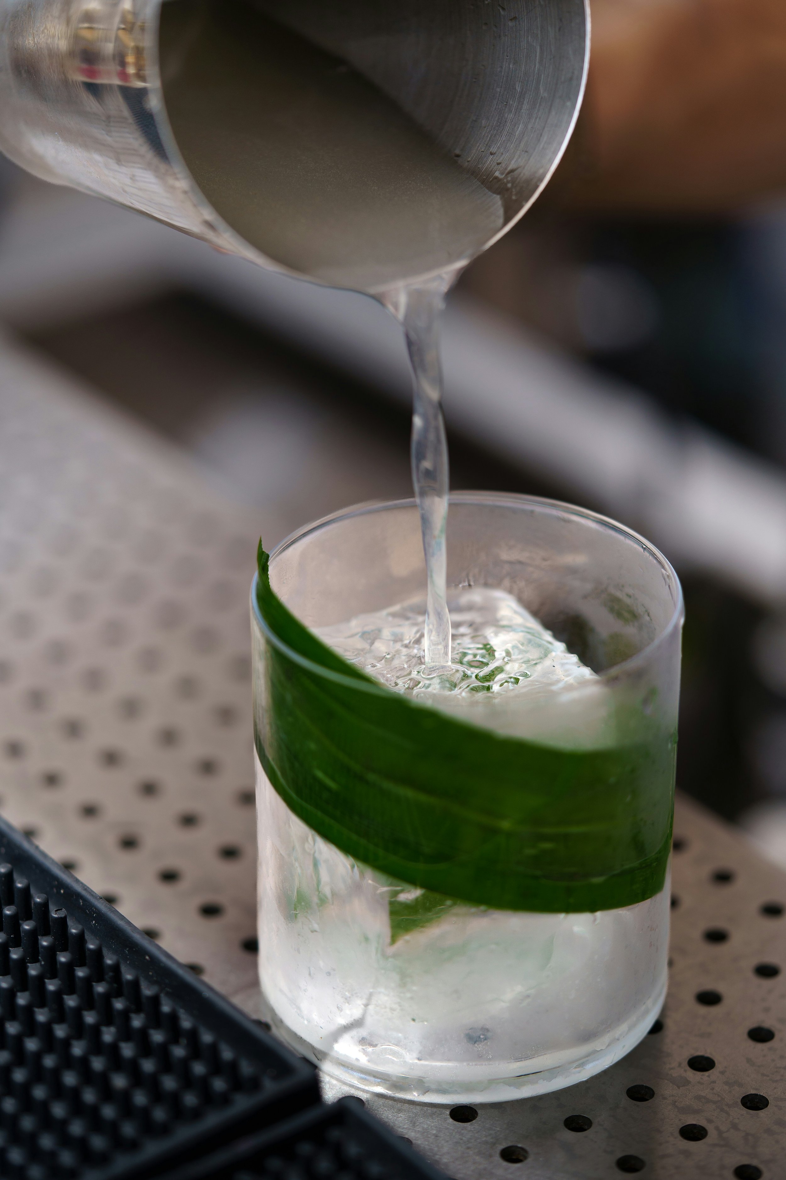 Nahaufnahme eines Glases mit grüner Pflanzenblatt-Dekoration, das mit Wasser gefüllt ist, während Wasser aus einem Metallrohr in das Glas läuft.