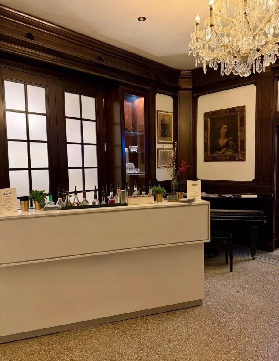Elegante Hotelbar mit Getränkeflaschen, Zimmerpflanzen, Kristallleuchter, dunkler Holzvertäfelung, Gemälden und Klavier