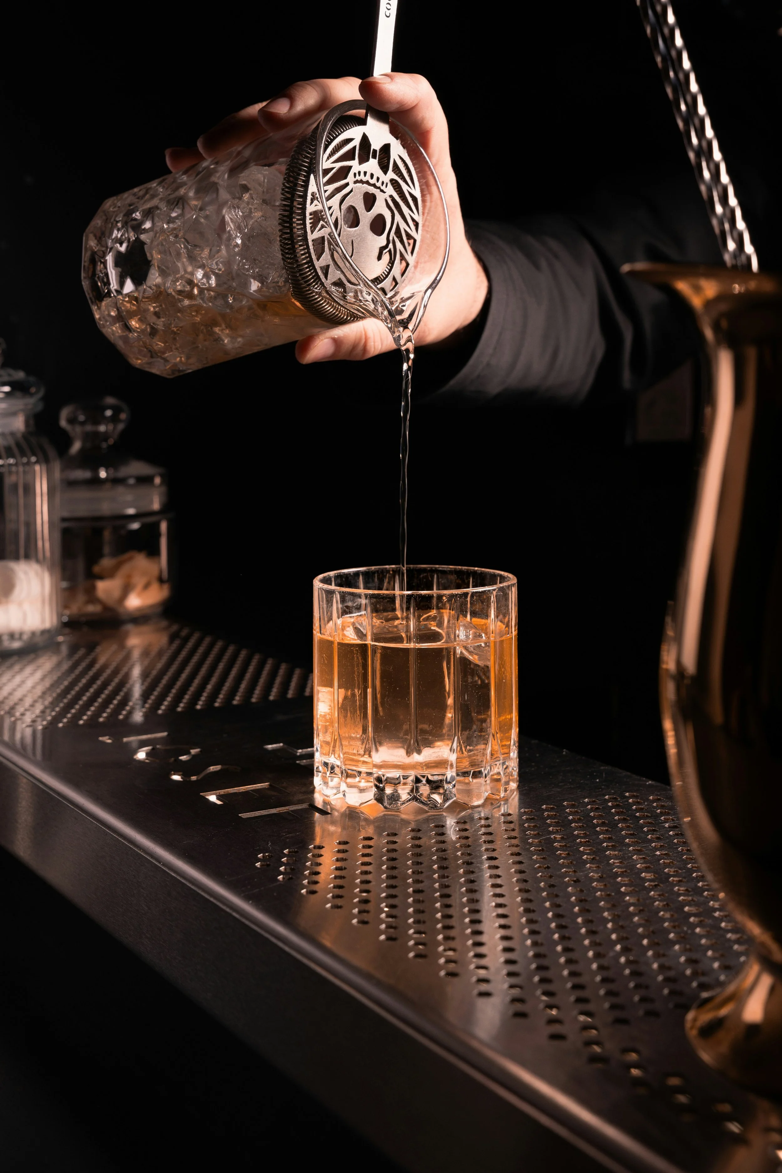 Ein Regal mit Gläsern und Flaschen hinter einer Espressomaschine, die einen Drink in ein Glas gießt.