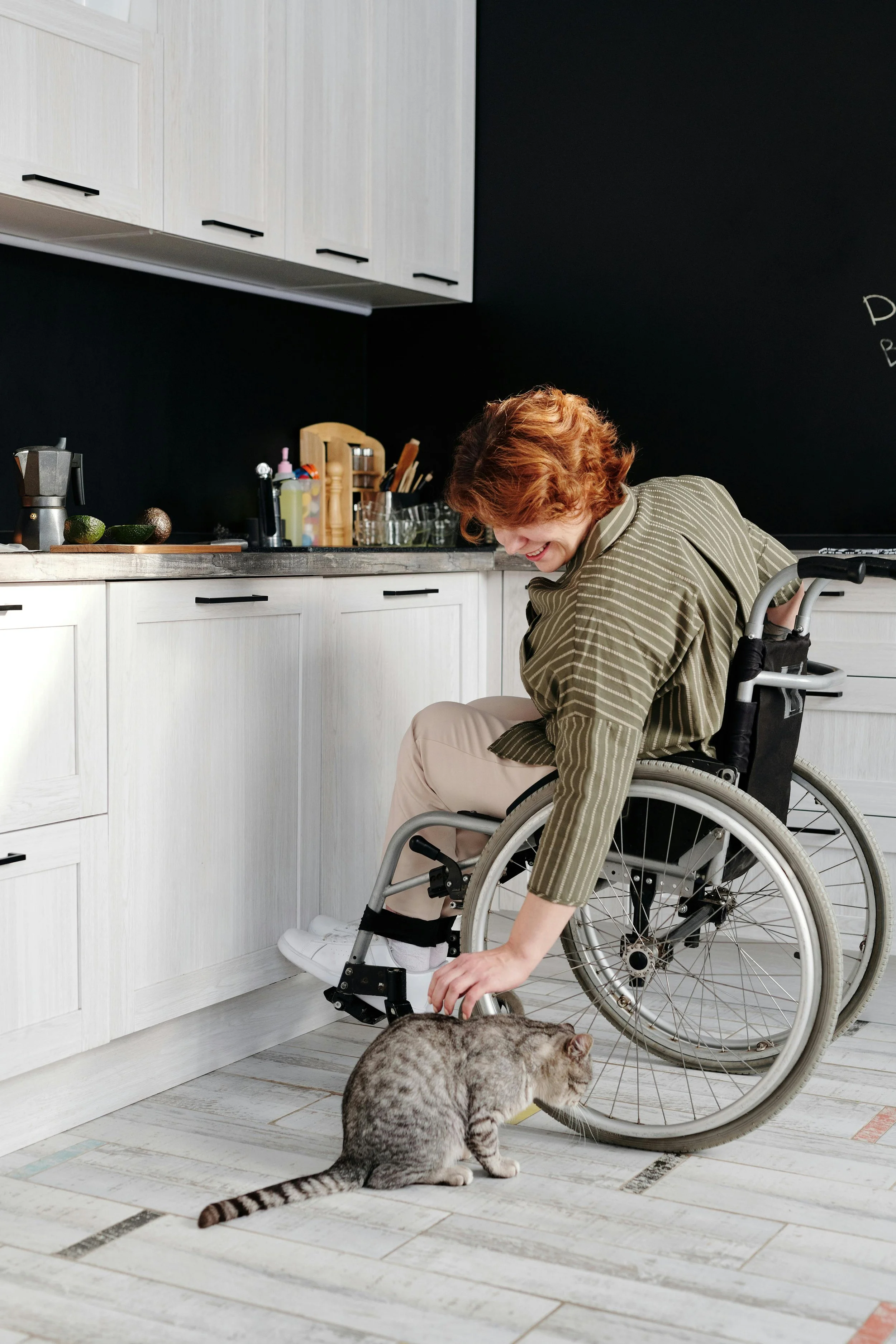 Woman in the kitchen using a wheelchair and petting a cat