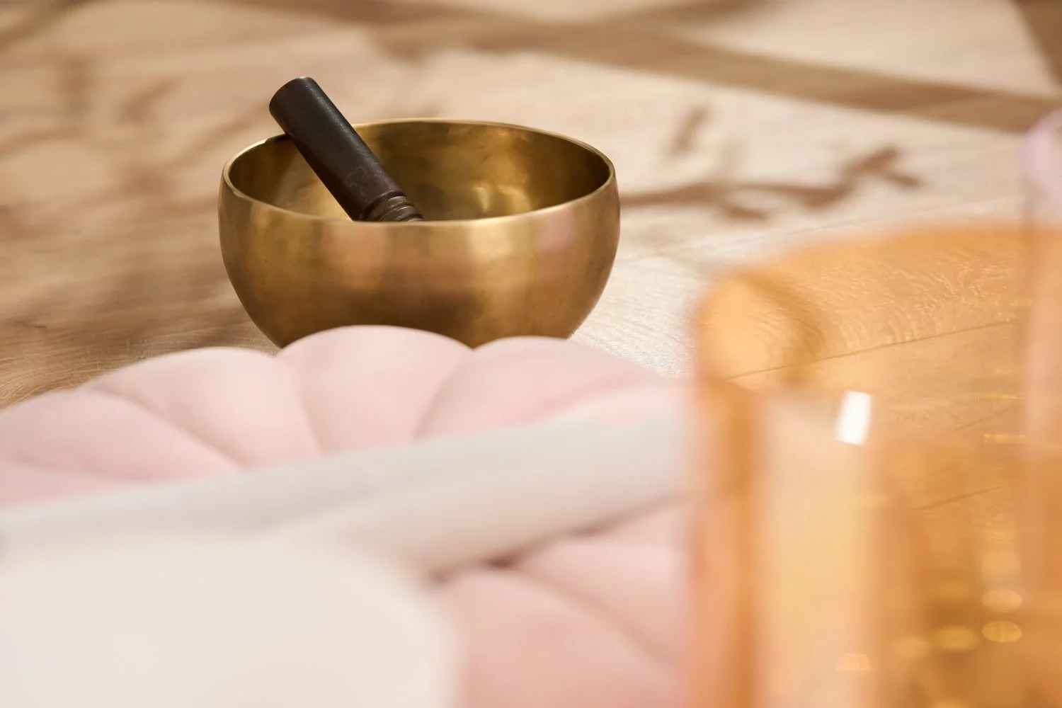 A Tibetan singing bowl with a wooden mallet resting inside on a wooden surface.