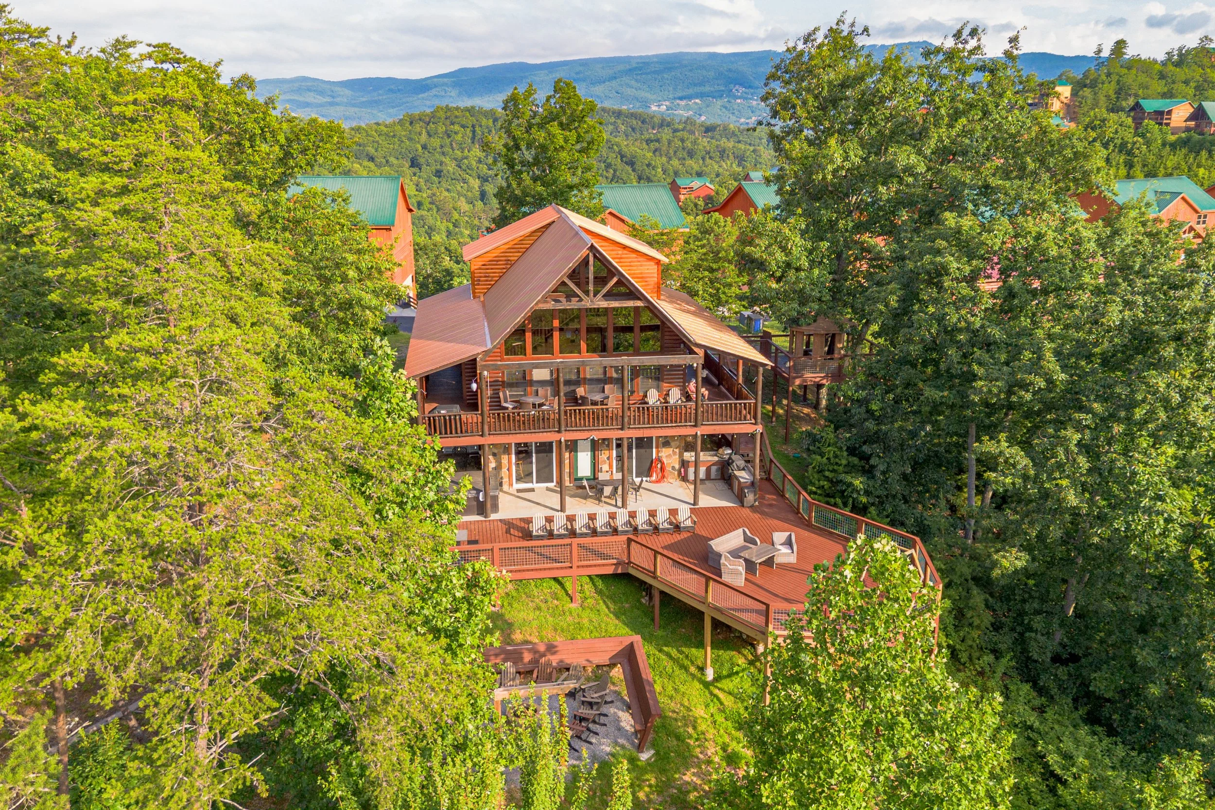 A large house on a hillside surrounded by trees, with a spacious deck and patio area.