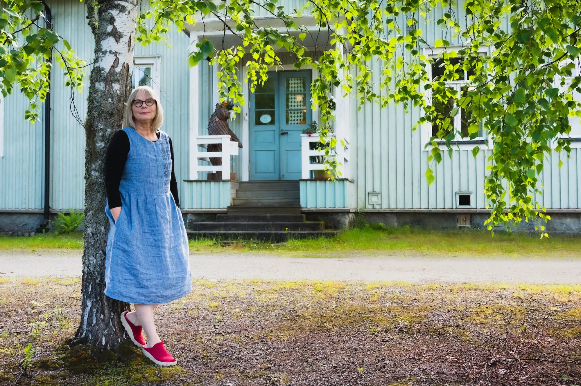 Nainen nojaa puuhun ja taustalla on kyläkoulu