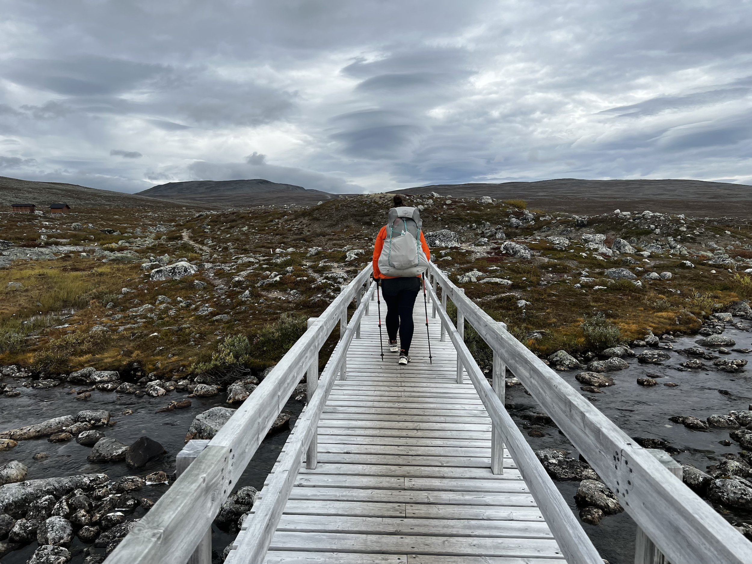 Nainen kävelee rinkka selässä sillalla avotunturissa