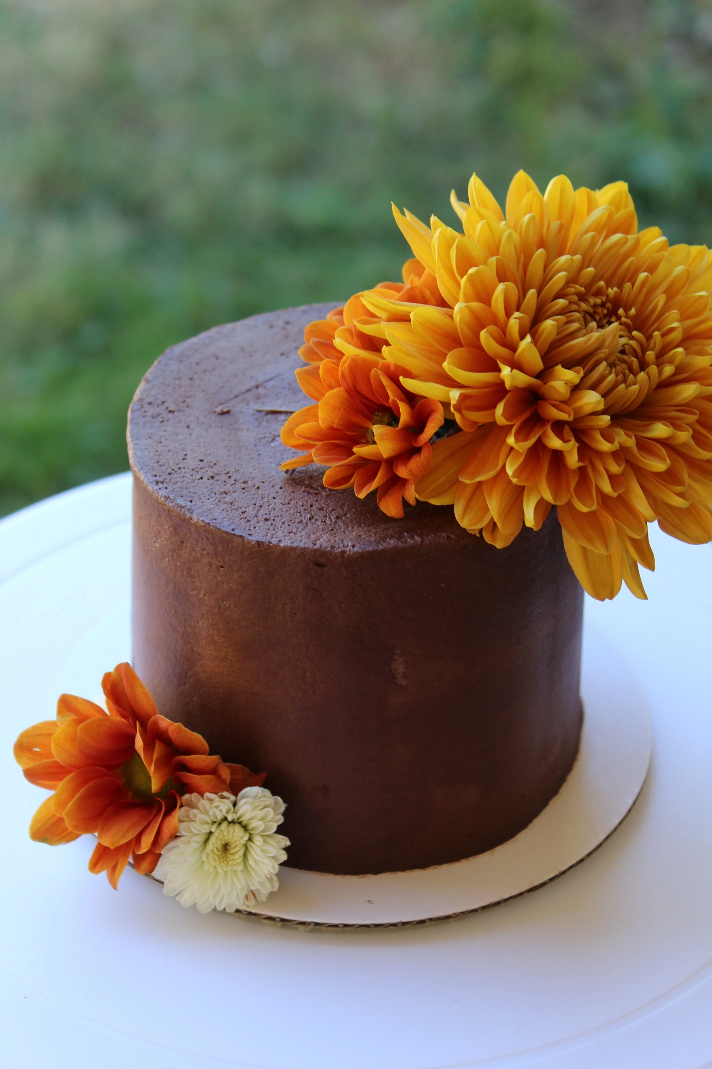 Chocolate cake decorated with orange and white flowers on top of a white cake board.