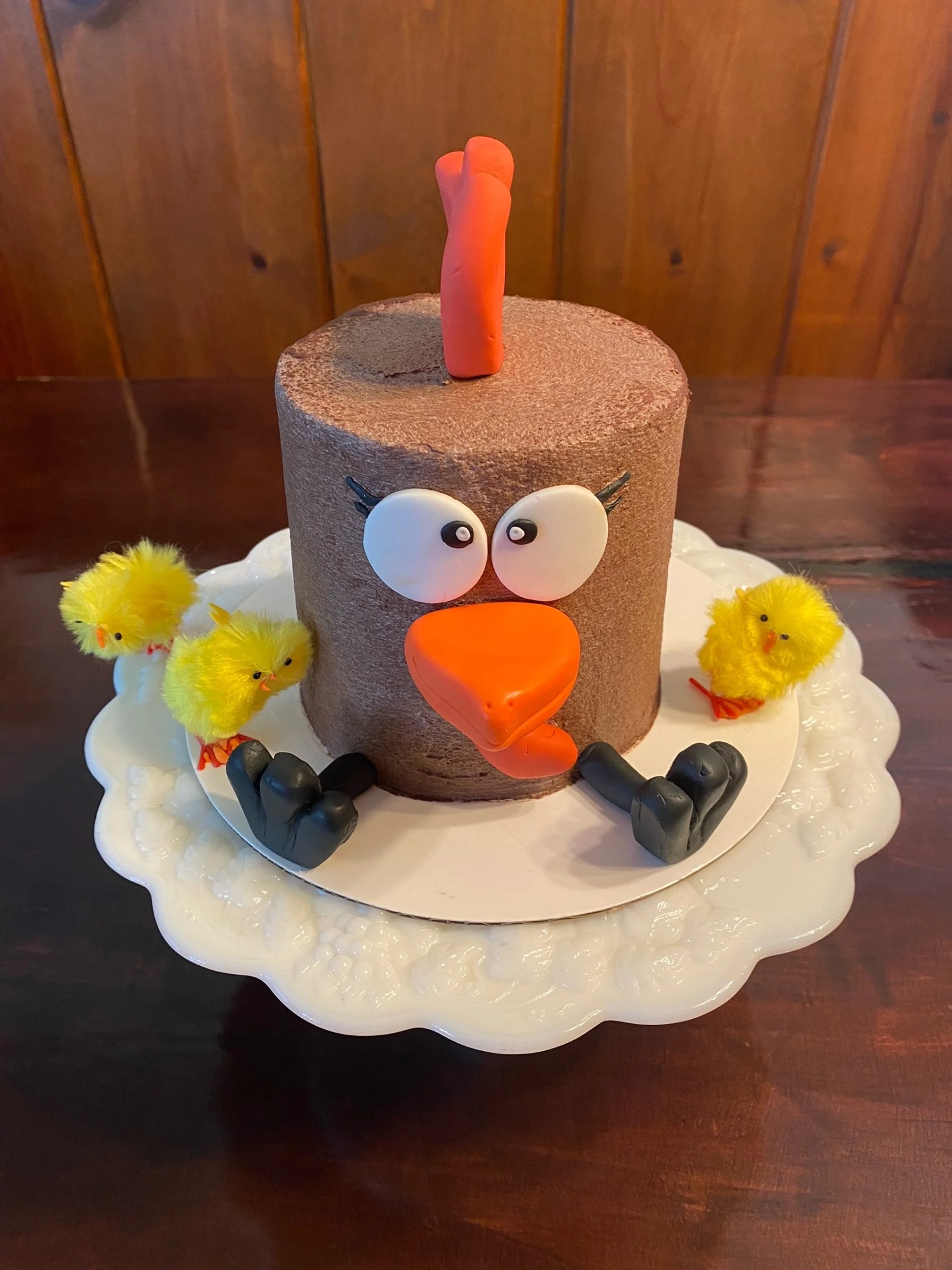 Cake decorated as a cartoon chicken with yellow chicks on a white plate.