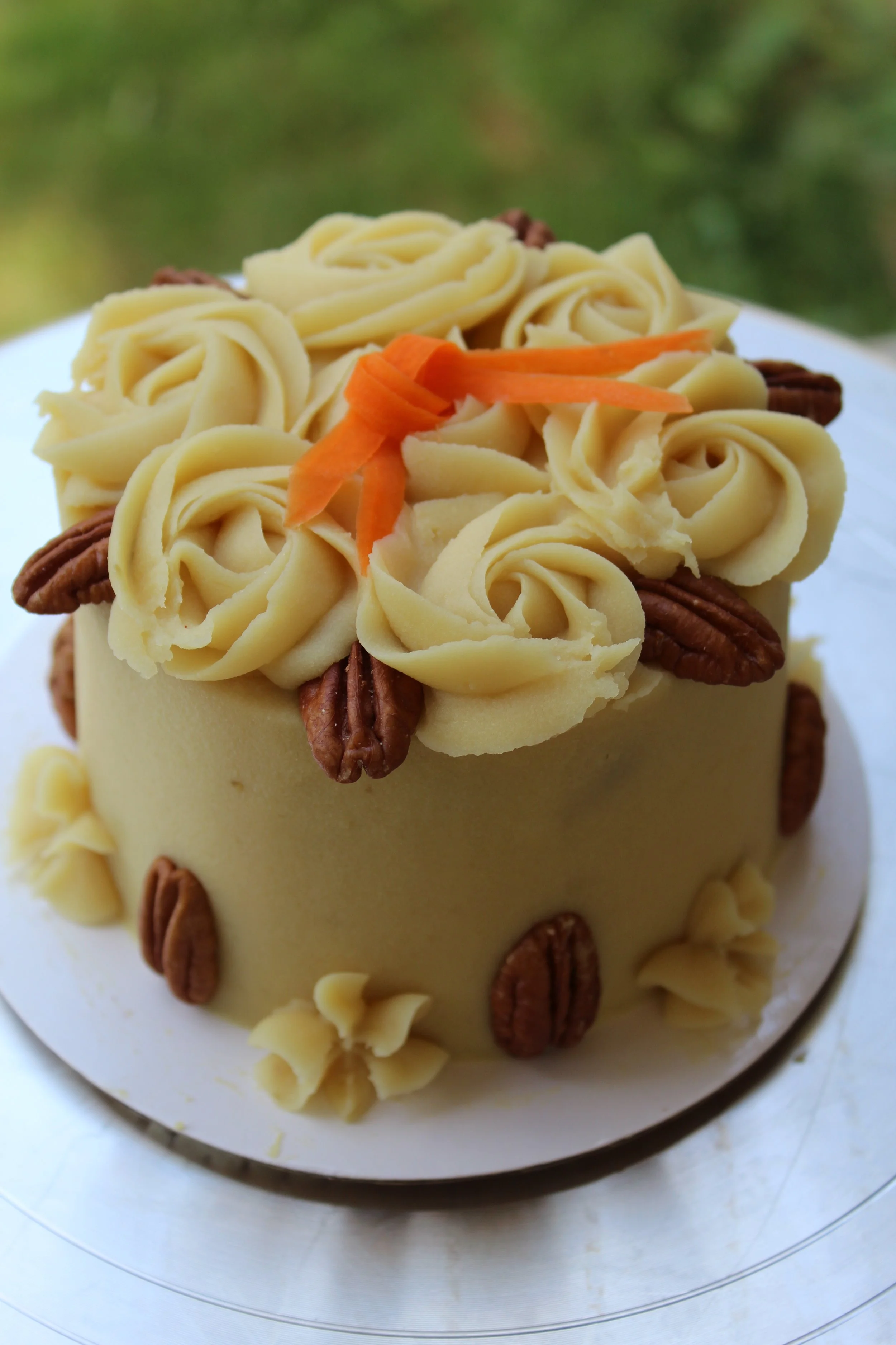 A round cake decorated with white chocolate rosettes, pecans, and a small garnish of orange carrots on top.