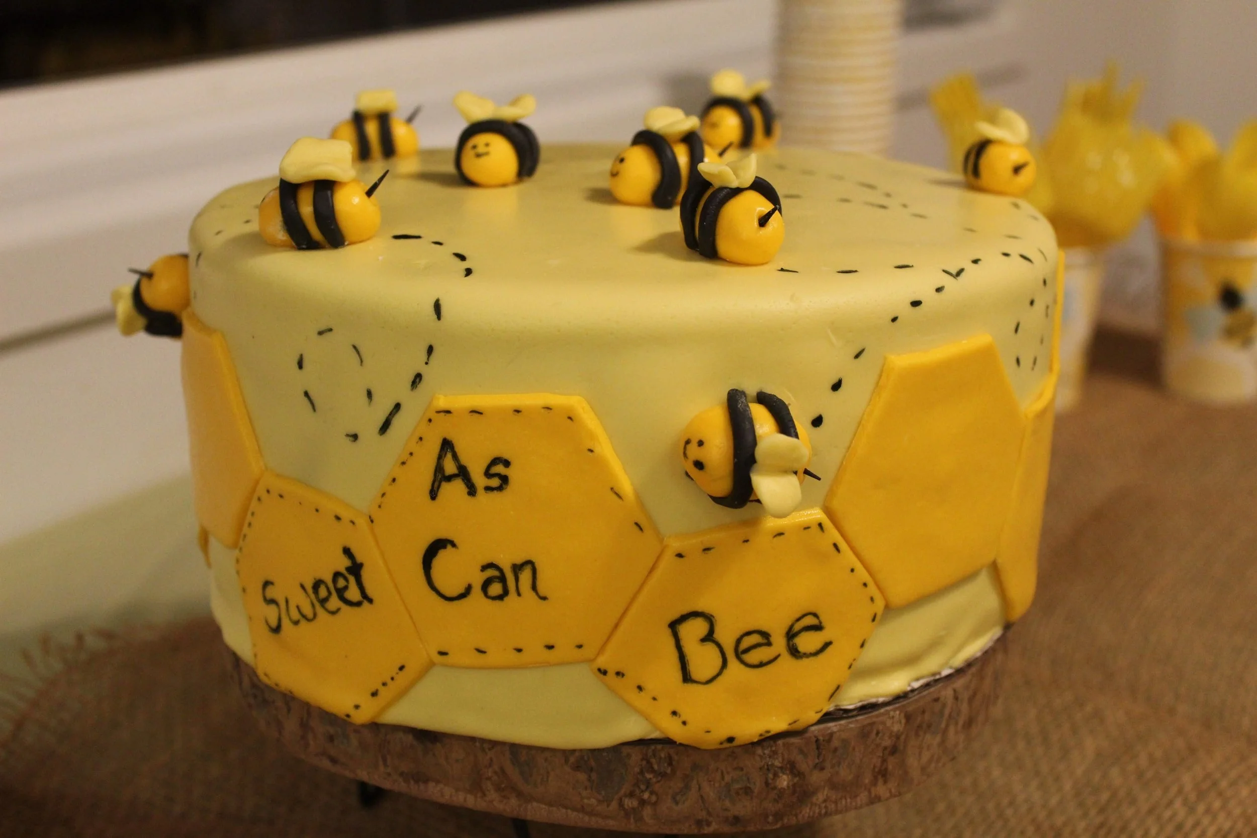 A honey-themed birthday cake decorated with honey bees, honeycomb shapes, and a message that reads 'Sweet As Can Bee'.
