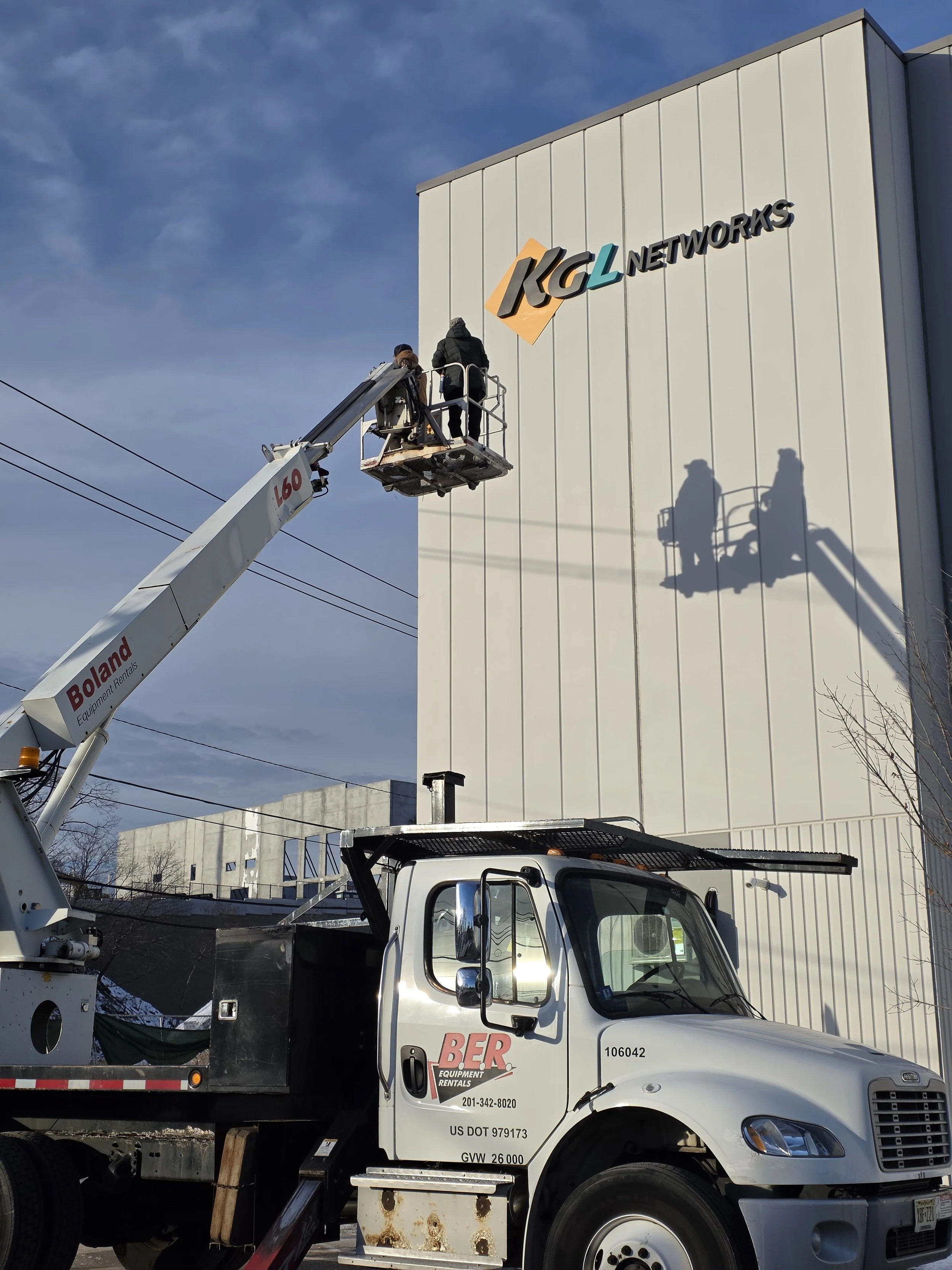 Workers on a lift installing a sign on the side of a building that reads 'KCL Networks'.
