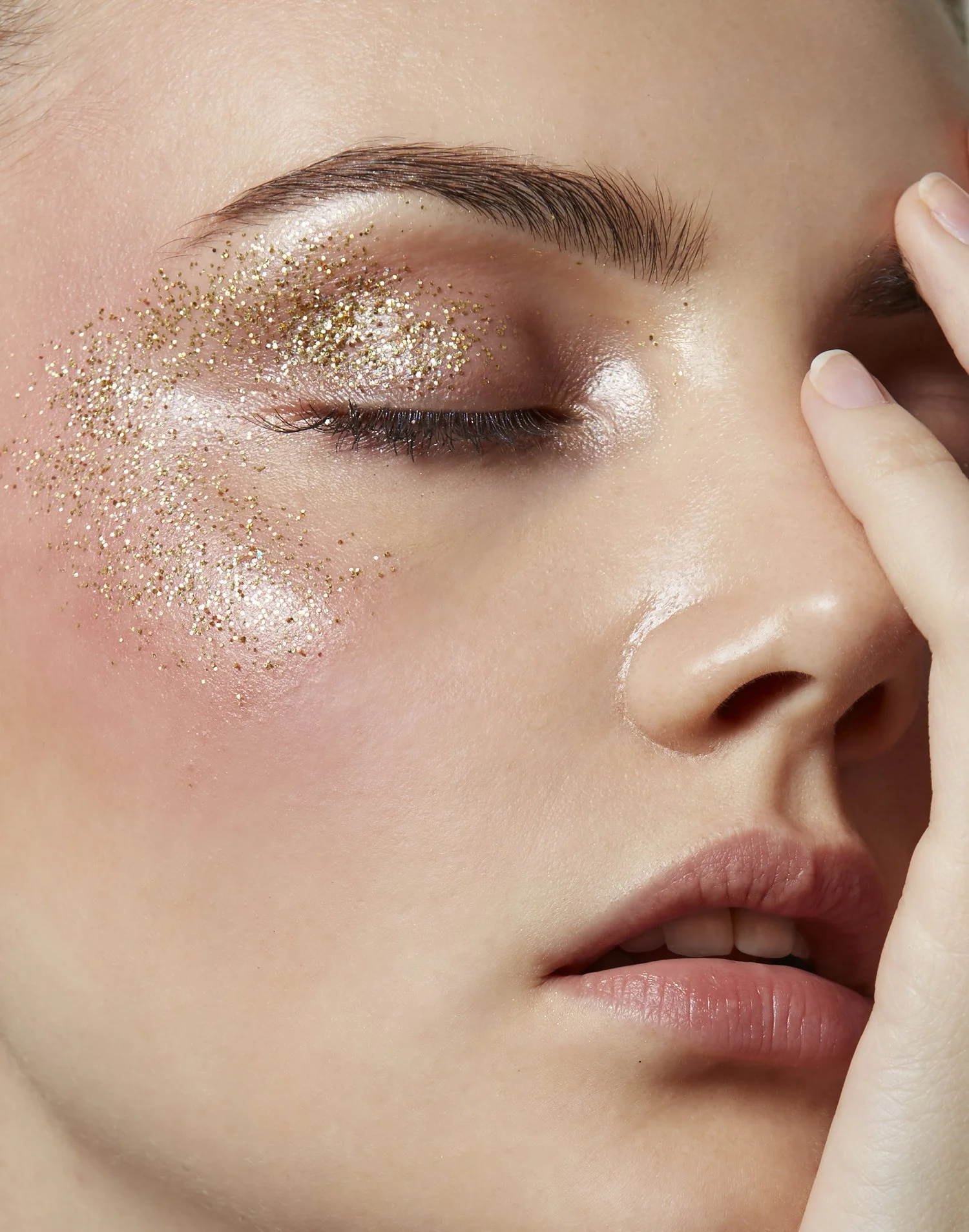 Close-up of a woman with glittery eye makeup and glossy skin