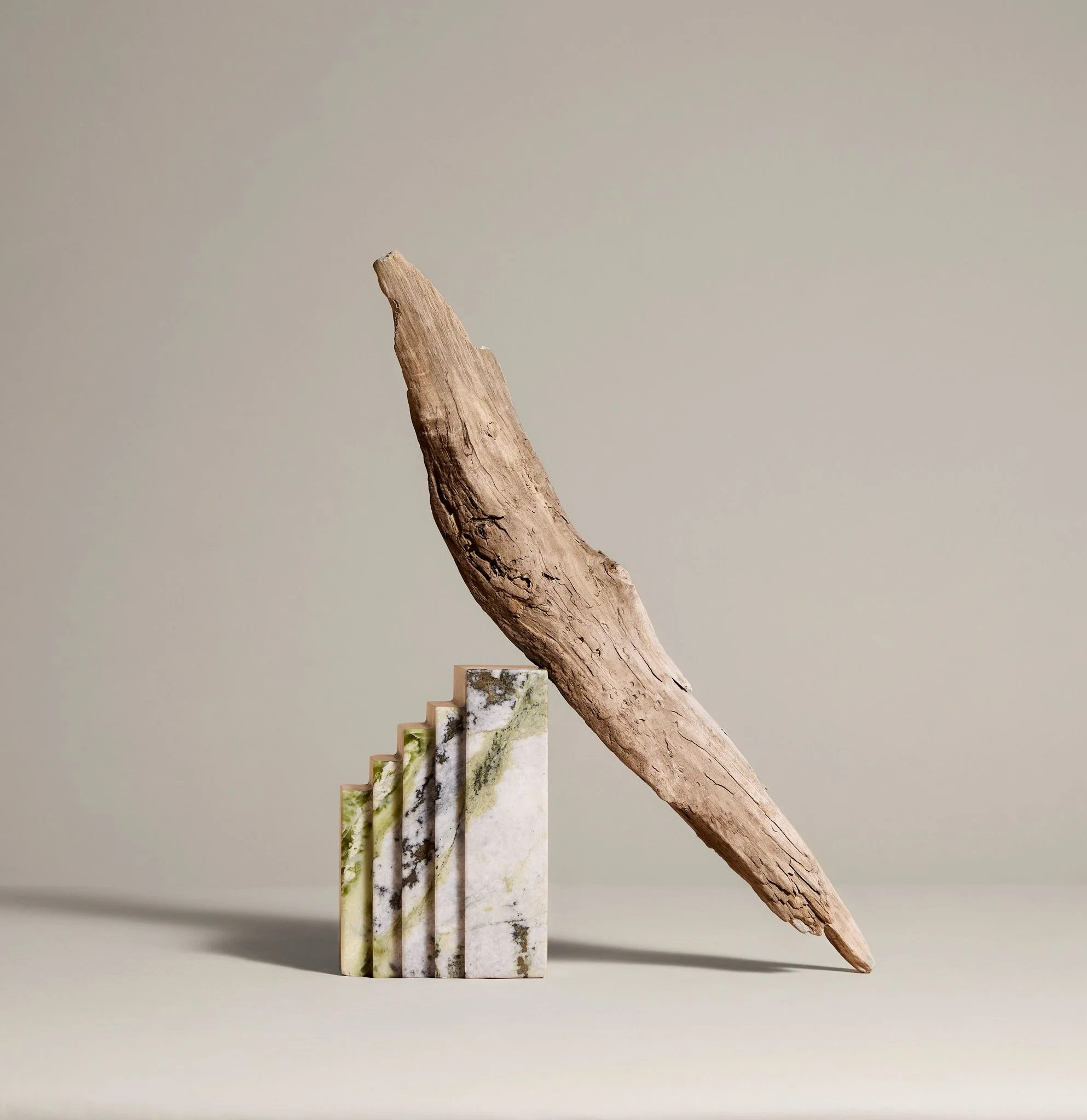 A piece of driftwood balanced on a stack of textured green and white marble slabs against a neutral background.