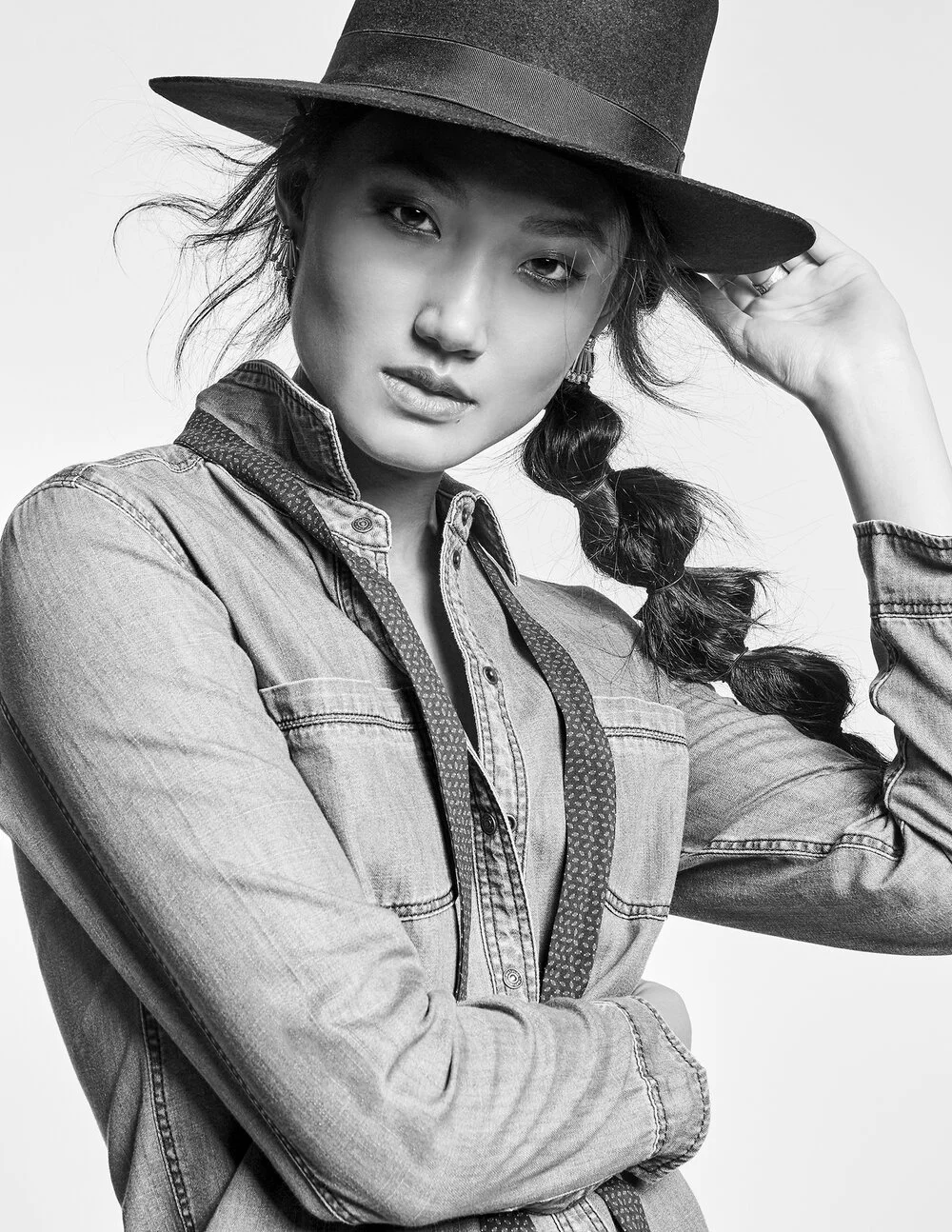 Black and white photo of a person wearing a denim shirt and a hat, posing with one hand on the hat.