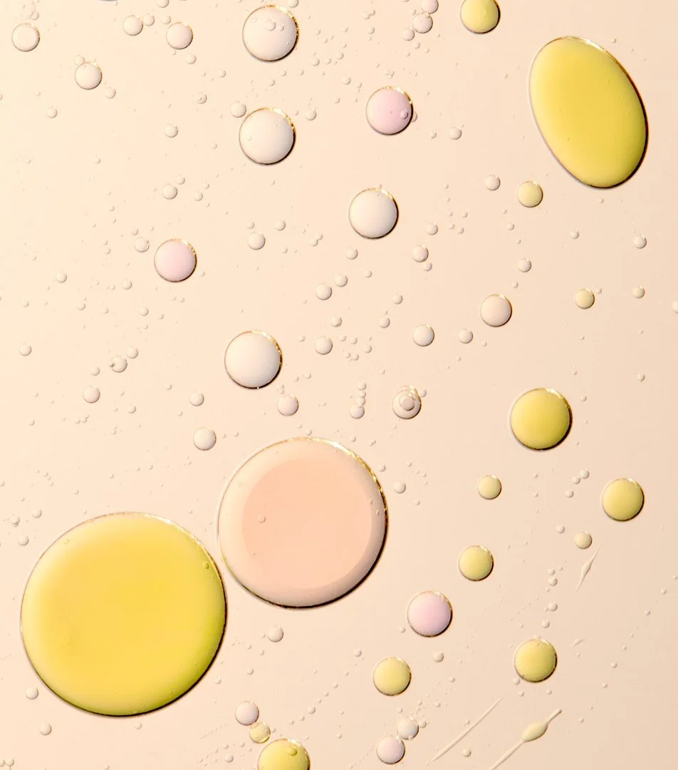 Abstract macro shot of cream and foundation droplets in beige, peach, and yellow tones, by Adrianna Favero.