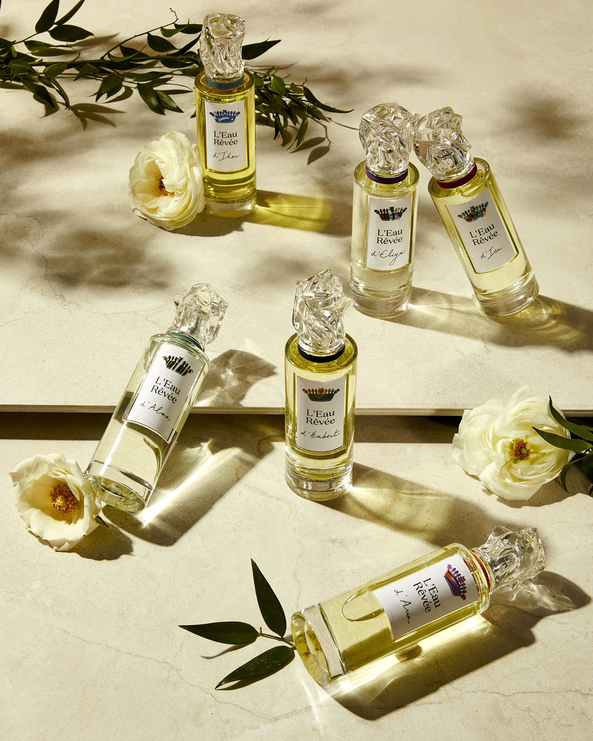 Perfume bottles labeled "L’Eau Rêvée" with floral and greenery accents on a light marble surface.