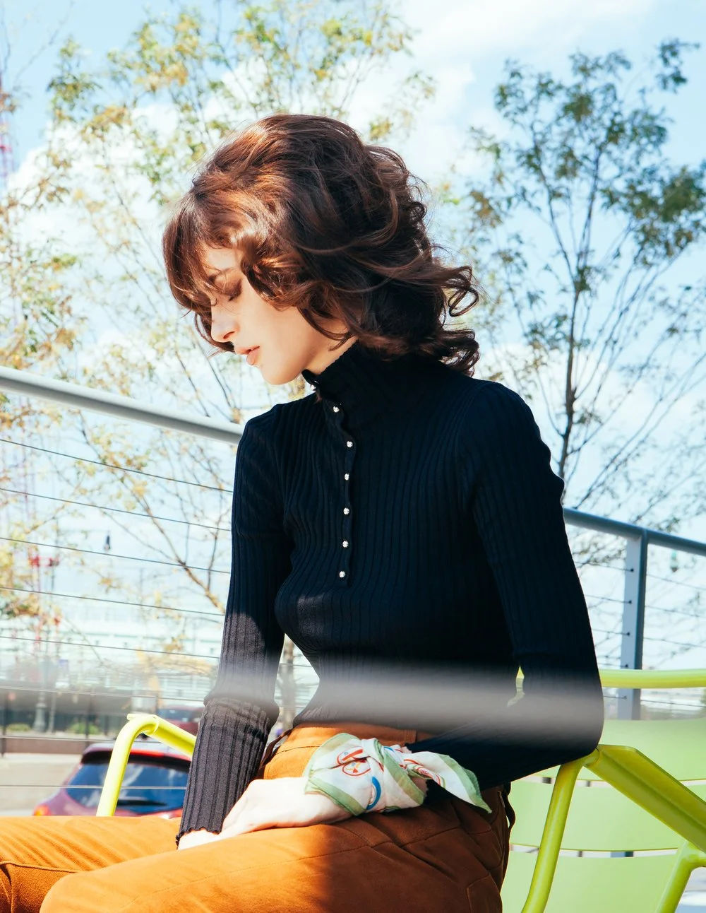 Woman with curly hair wearing black turtleneck seated outdoors
