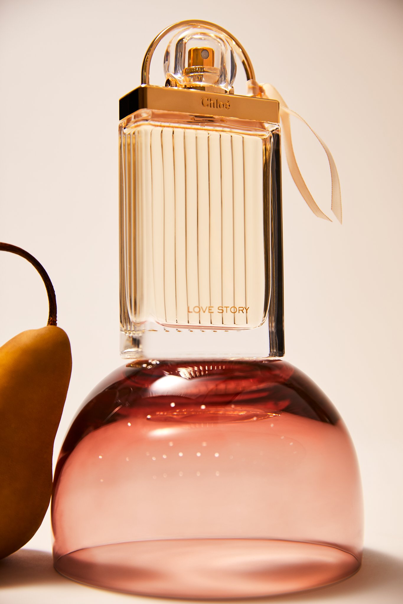Perfume bottle with "Love Story" label, atop a pink glass dome, next to a pear.