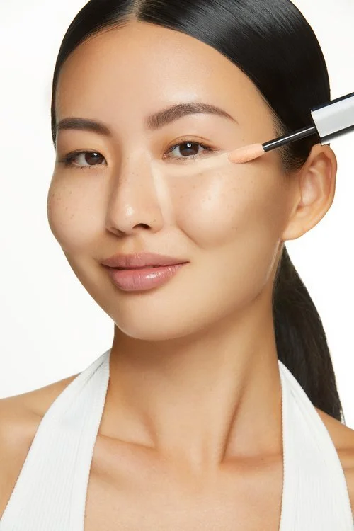 Lancome complexion makeup tutorial: model applying concealer beneath the eye with a precision brush, photographed by Adrianna Favero.