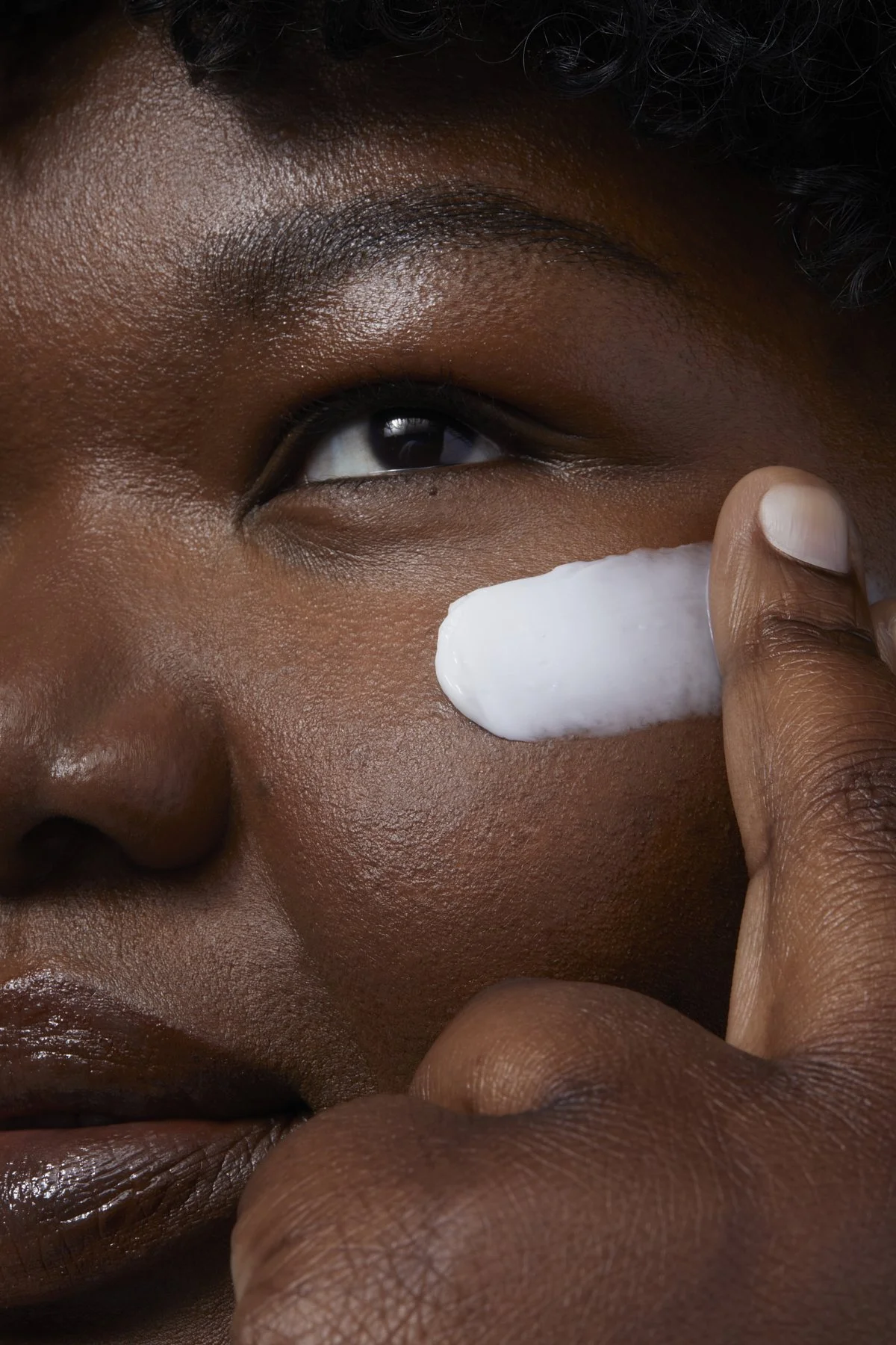 Beauty close-up of a model with deep, glowing skin applying a peptide cream near her eye, demonstrating a hydrating skincare routine for a beauty brand campaign by Adrianna Favero, NYC beauty photographer and director.