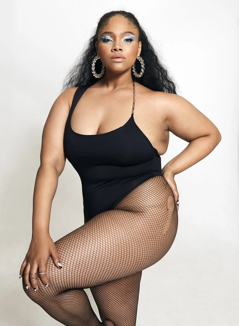 Woman in black outfit with fishnet stockings, large earrings, and bold makeup.