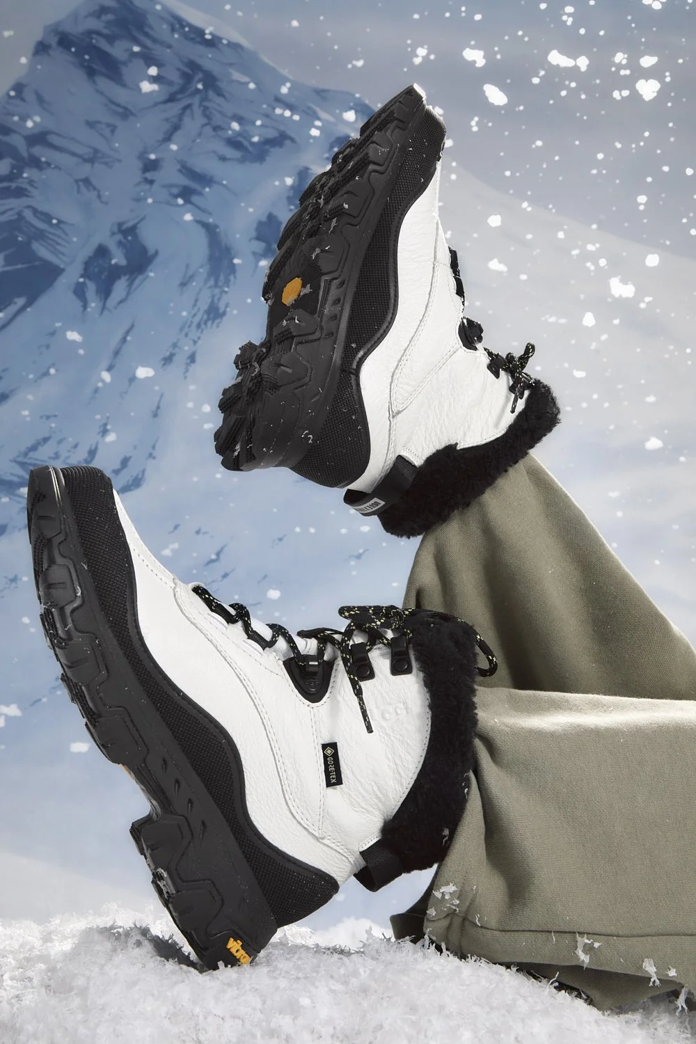 Pair of white winter boots with black soles in the snow, mountain backdrop