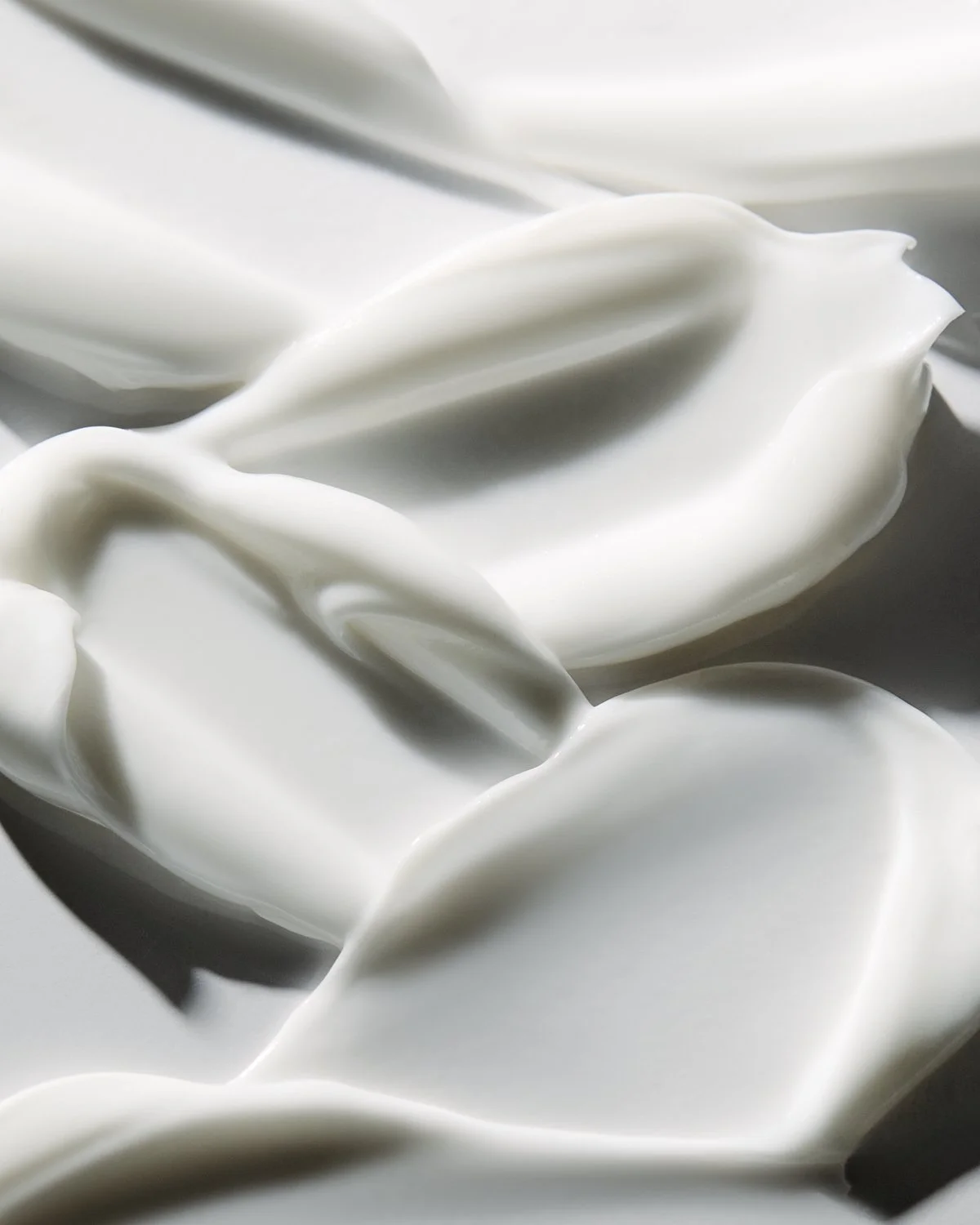 Close-up texture shot of smooth white cream swirled into soft waves, by Adrianna Favero.