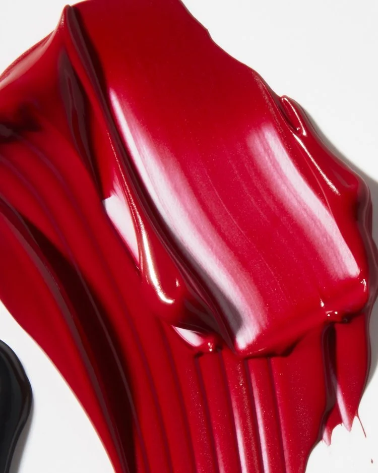 Close-up texture shot of glossy red lip gloss smeared on a dark surface, by Adrianna Favero.