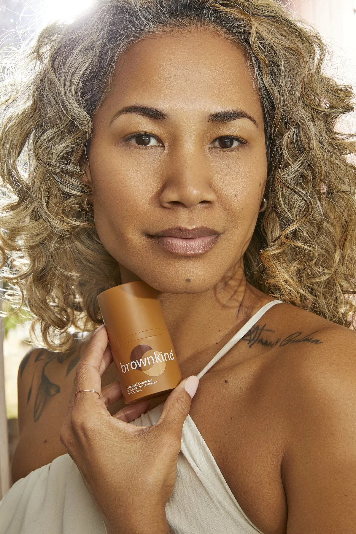 Beauty photography of a mature model with curly hair holding a foundation bottle near her face, showcasing an inclusive skincare and cosmetics product for a beauty brand campaign by Adrianna Favero, NYC beauty photographer and director.