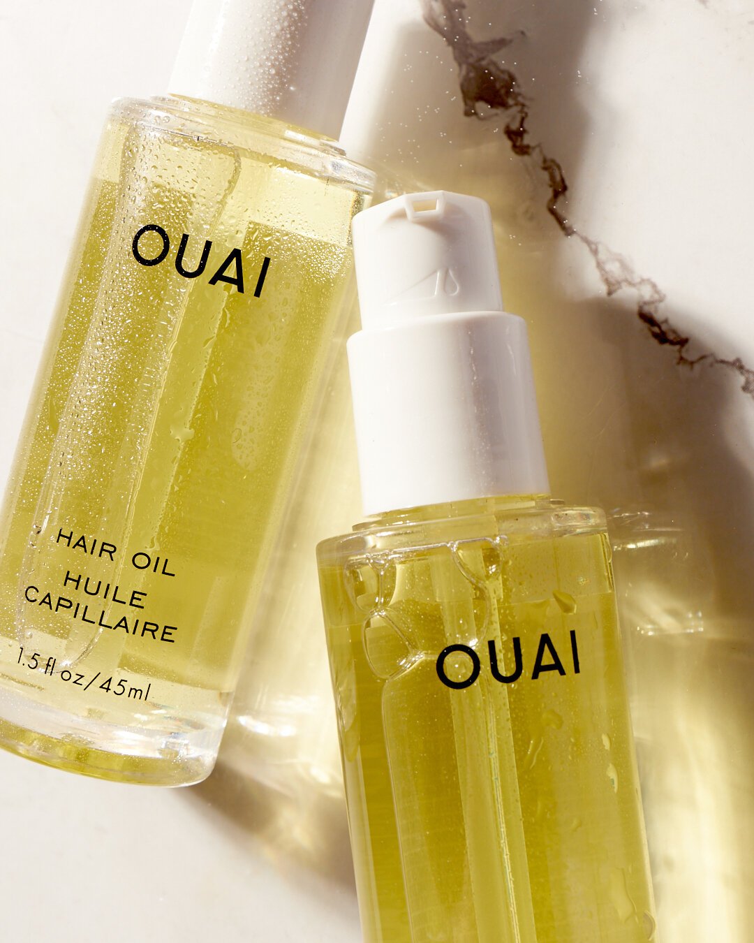 Two bottles of Ouai hair oil on a marble surface