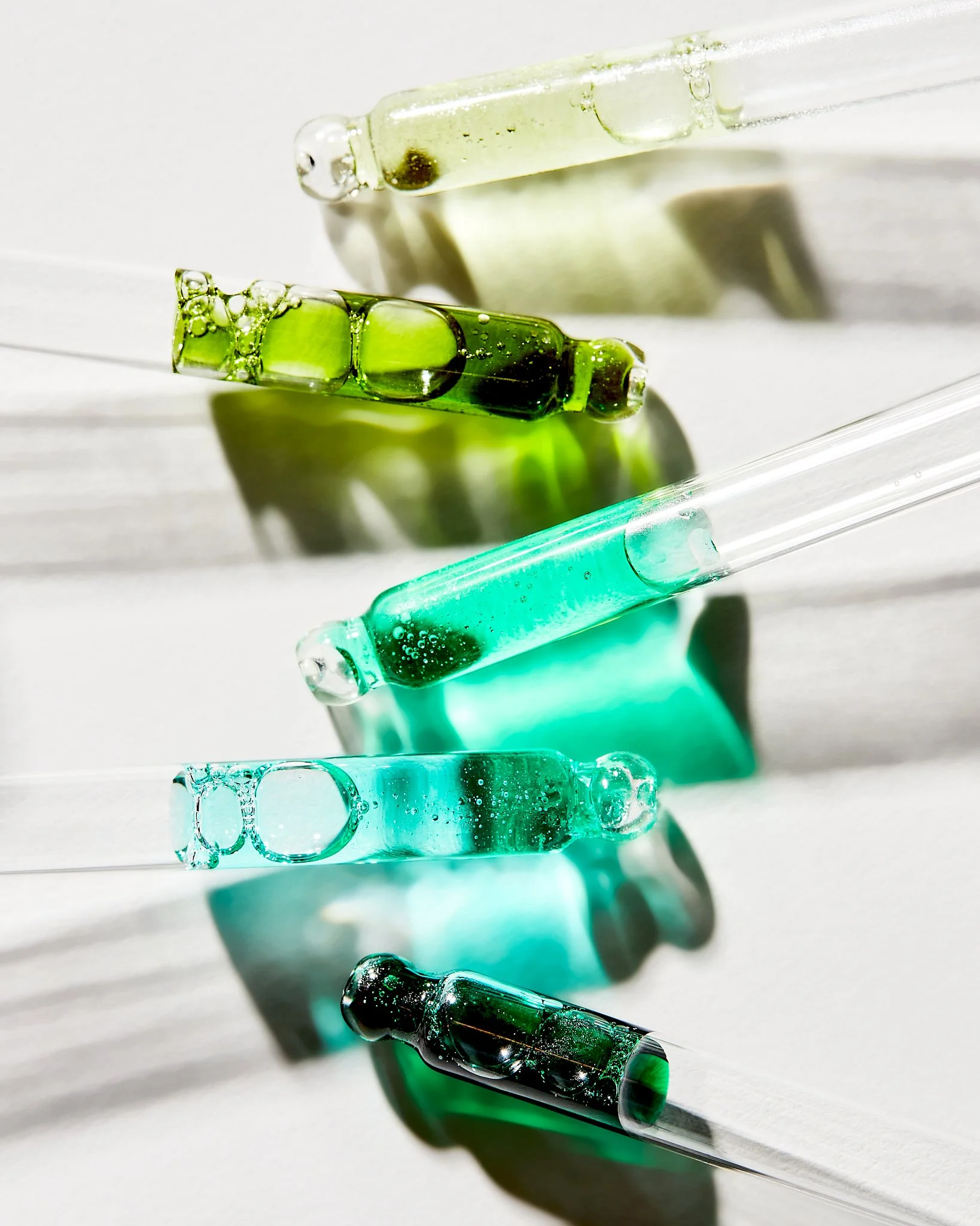 Assorted glass pipettes with green and blue liquids inside on a white background.