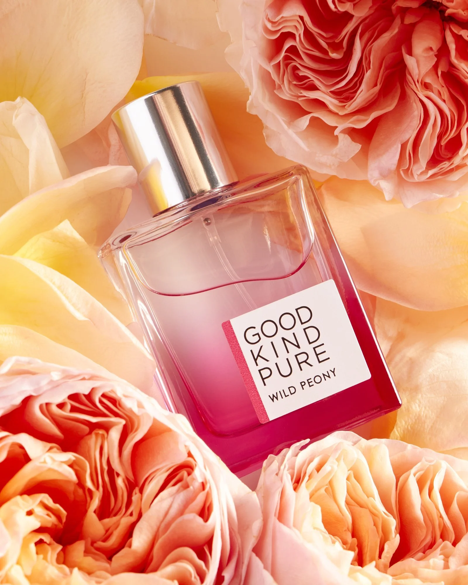 Perfume bottle labeled "Good Kind Pure Wild Peony" surrounded by pink and yellow peony flowers.