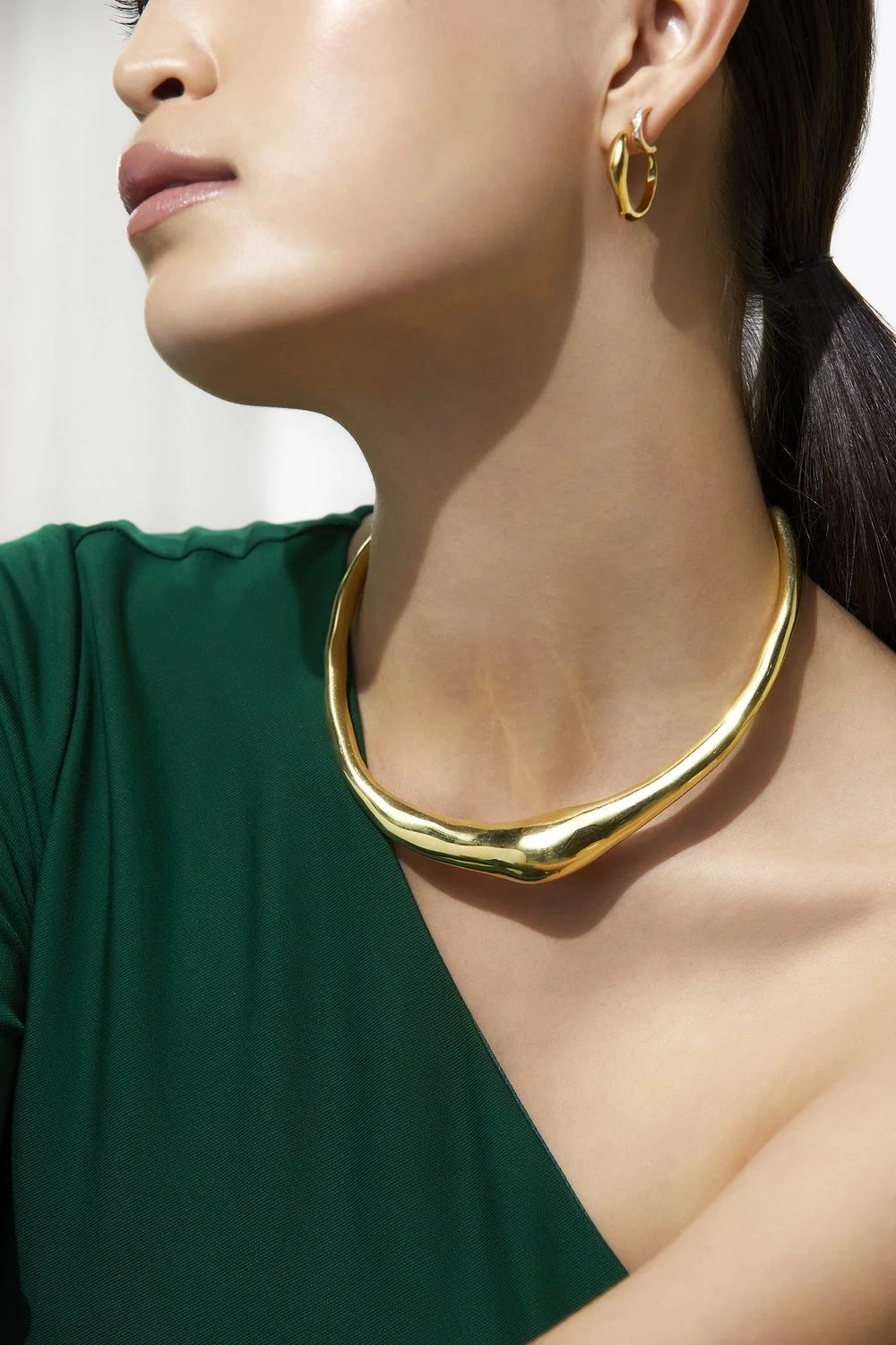 Woman wearing a gold necklace and hoop earring, dressed in a green top.