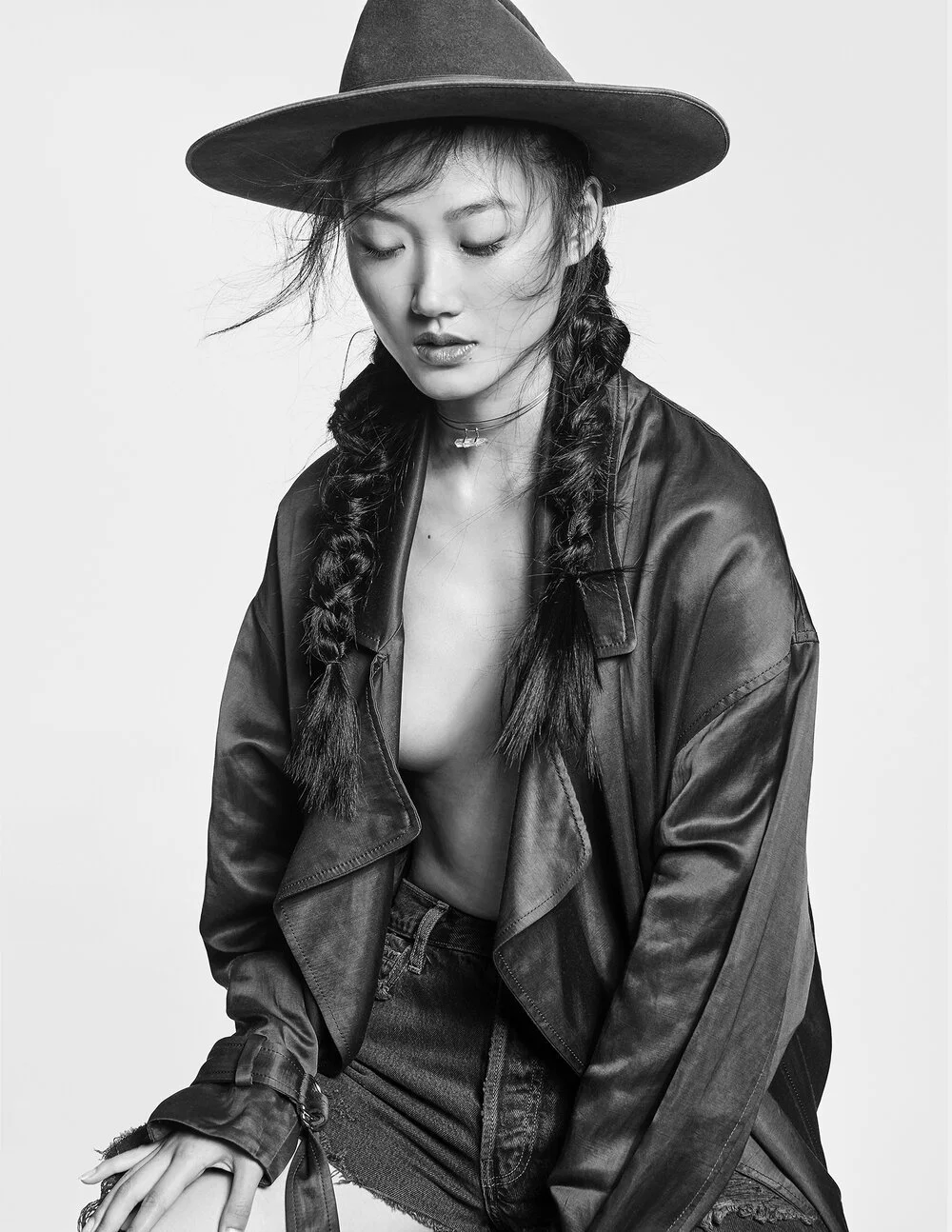 Black and white portrait of a person with two braids, wearing a hat and jacket, looking down.