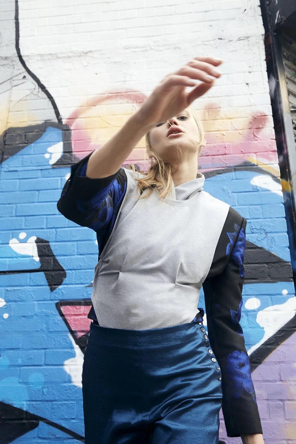 Fashionable person wearing mixed-material clothing posing in front of colorful graffiti.