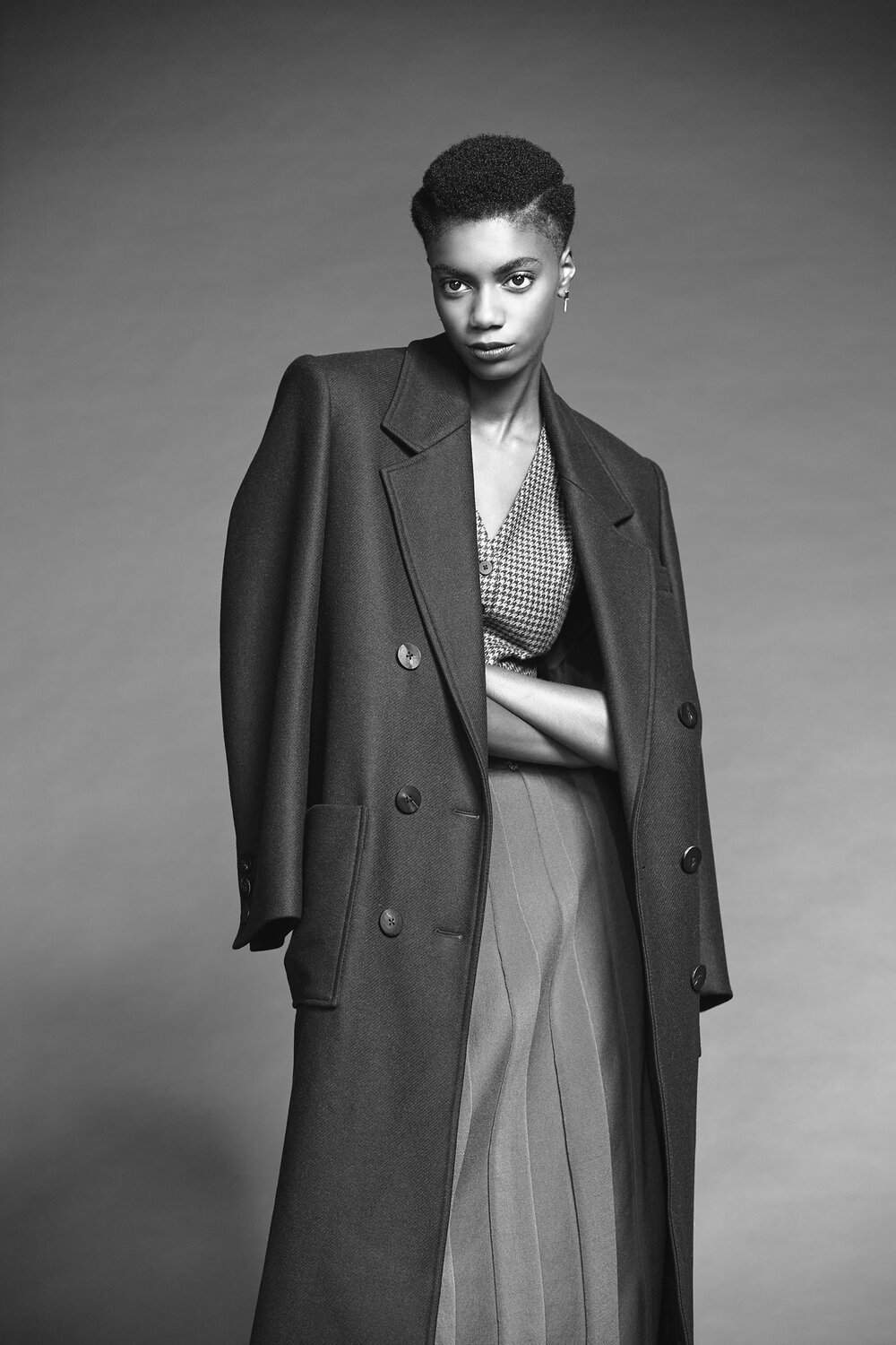 Black and white portrait of a person wearing a long coat and patterned blouse.
