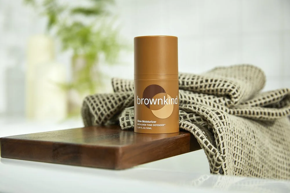 Product still life of a brow serum bottle on a wood stand with a woven towel backdrop, by Adrianna Favero.