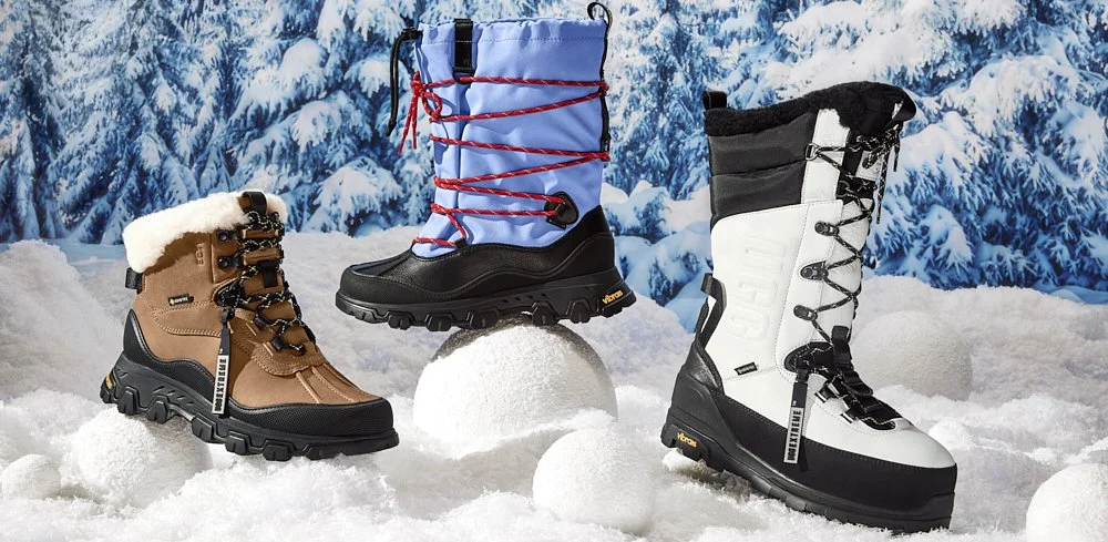 Three pairs of winter boots on snow with pine tree background. Left: brown boot with fur lining. Middle: blue boot with red laces. Right: black and white boot.