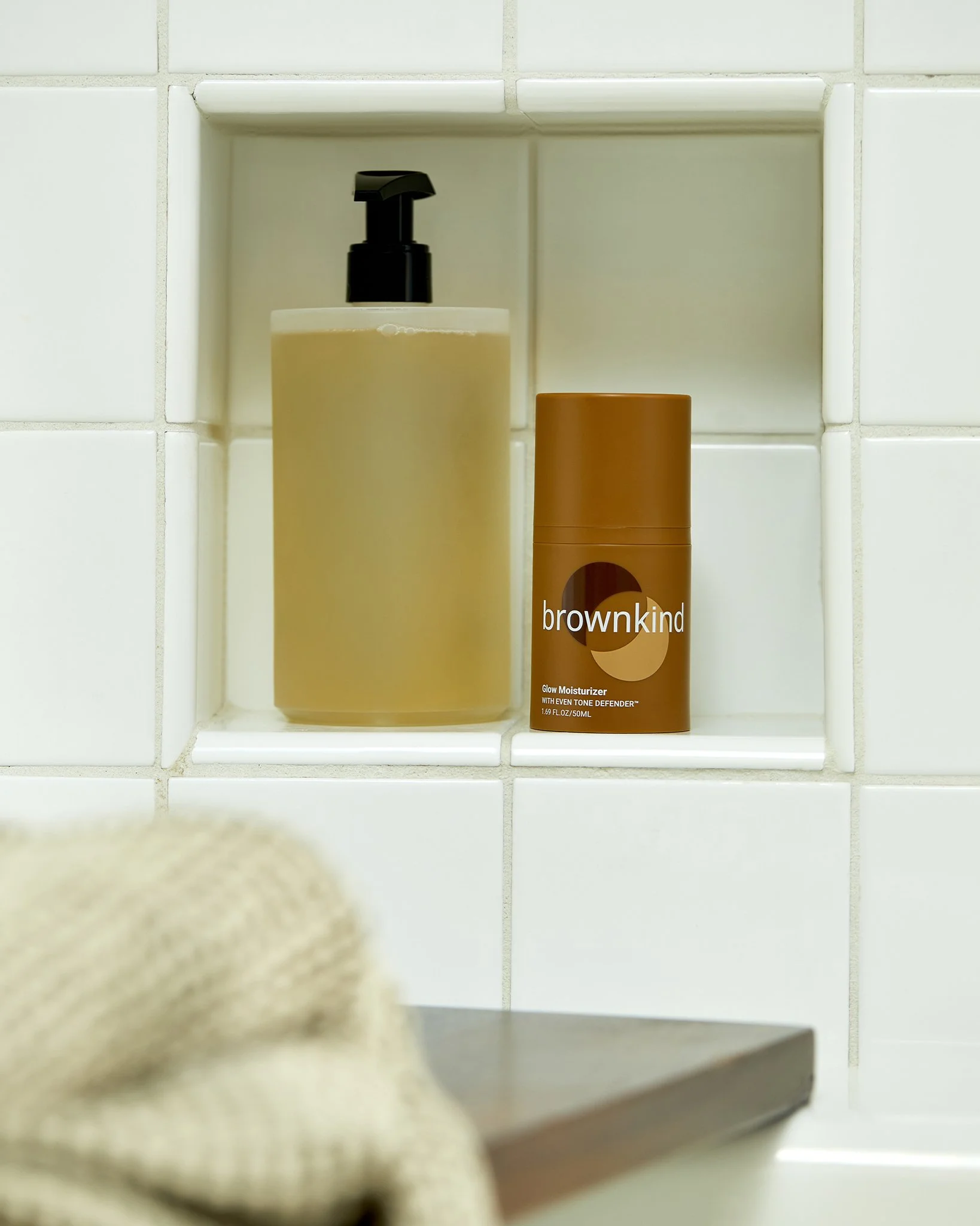 Still life of amber and cream skincare bottles displayed on a tiled shelf with a folded towel, by Adrianna Favero.