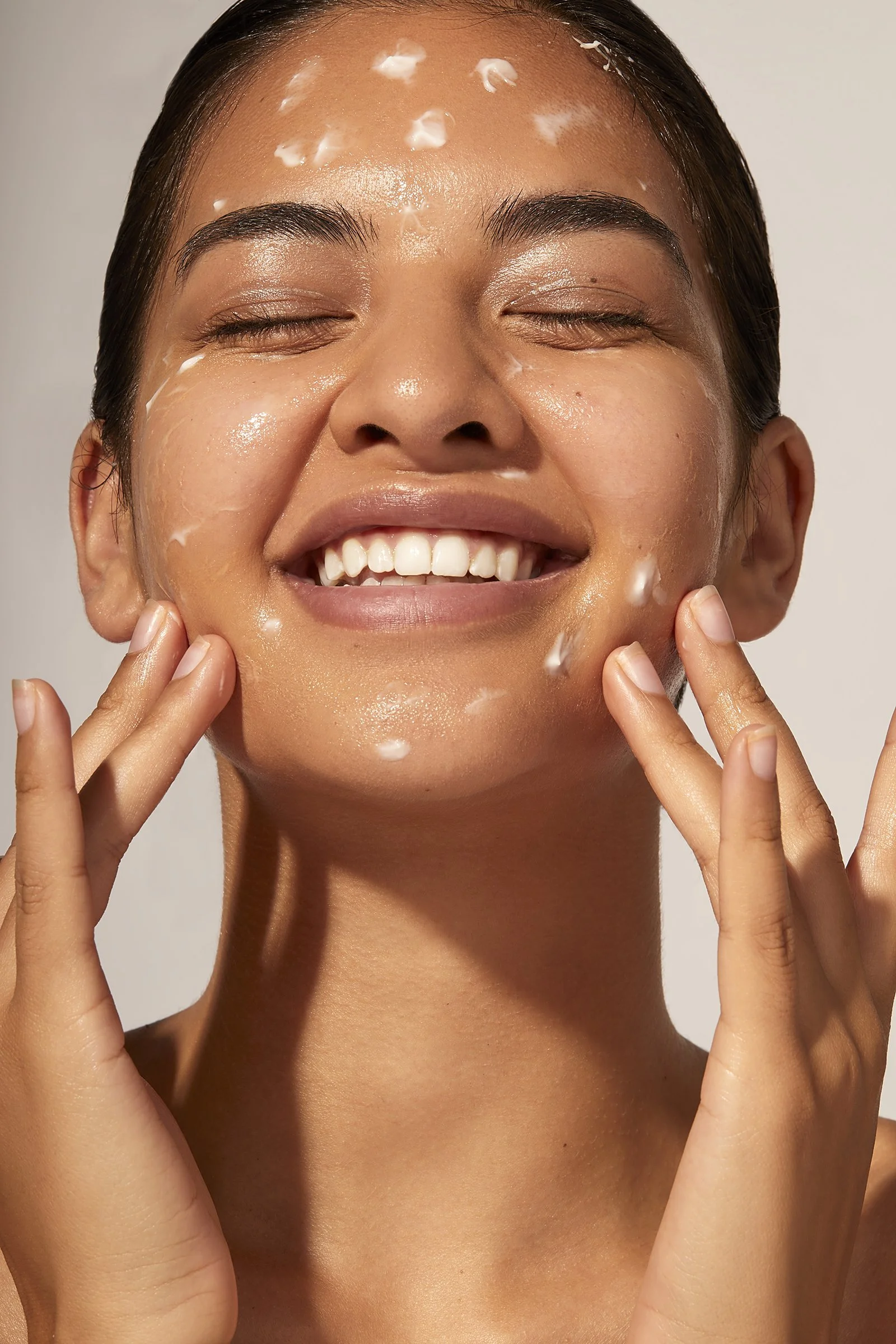 Person applying skincare cream on face with a joyful expression.