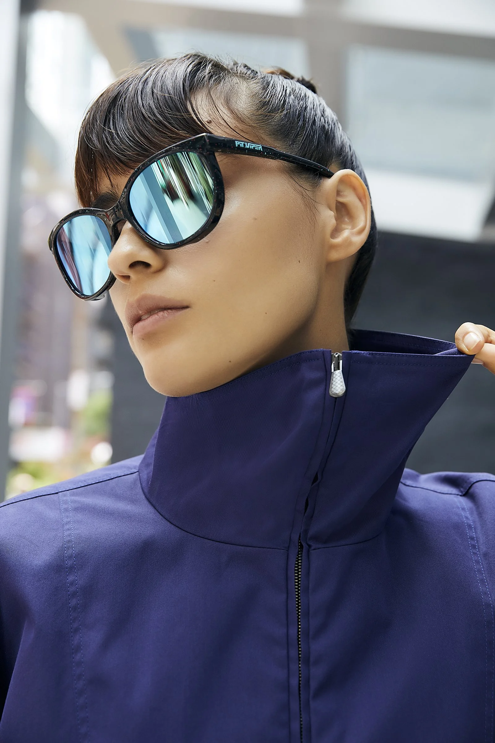 Person wearing reflective sunglasses and a blue high-collar jacket.