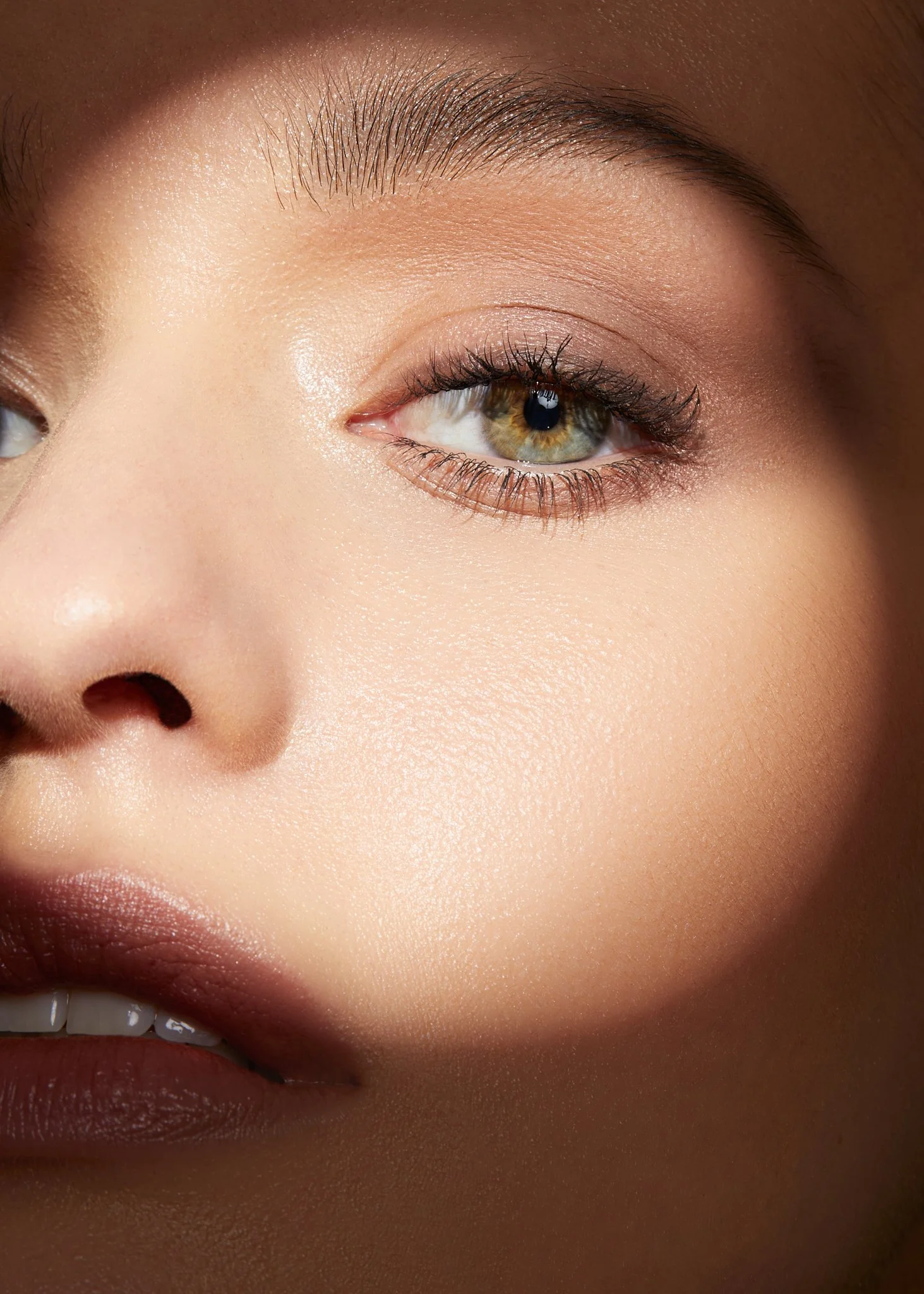 Close-up of a woman's face focusing on her eye, eyebrow, and part of her mouth, highlighting smooth skin and natural makeup.